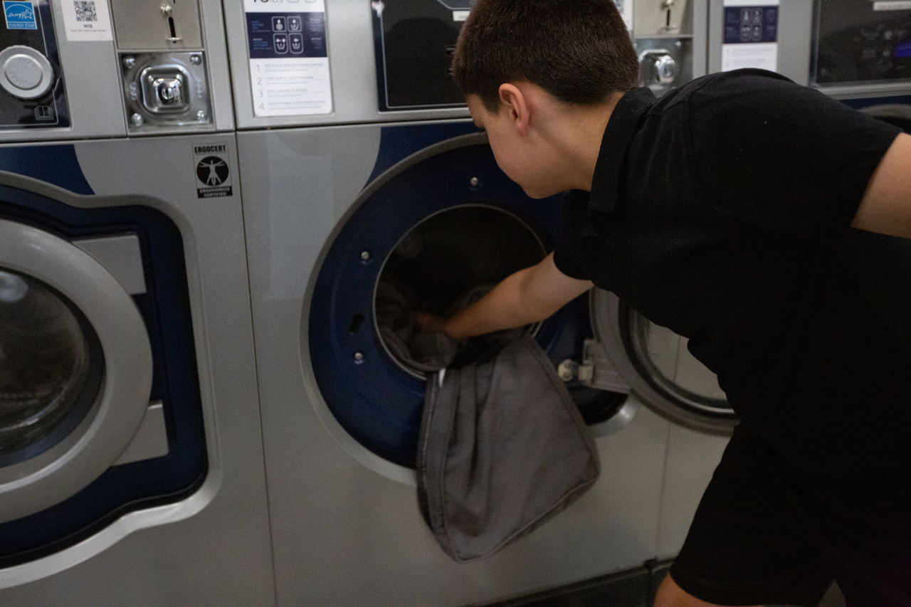 A person loading laundry into a coin-operated washing machine at a laundromat.