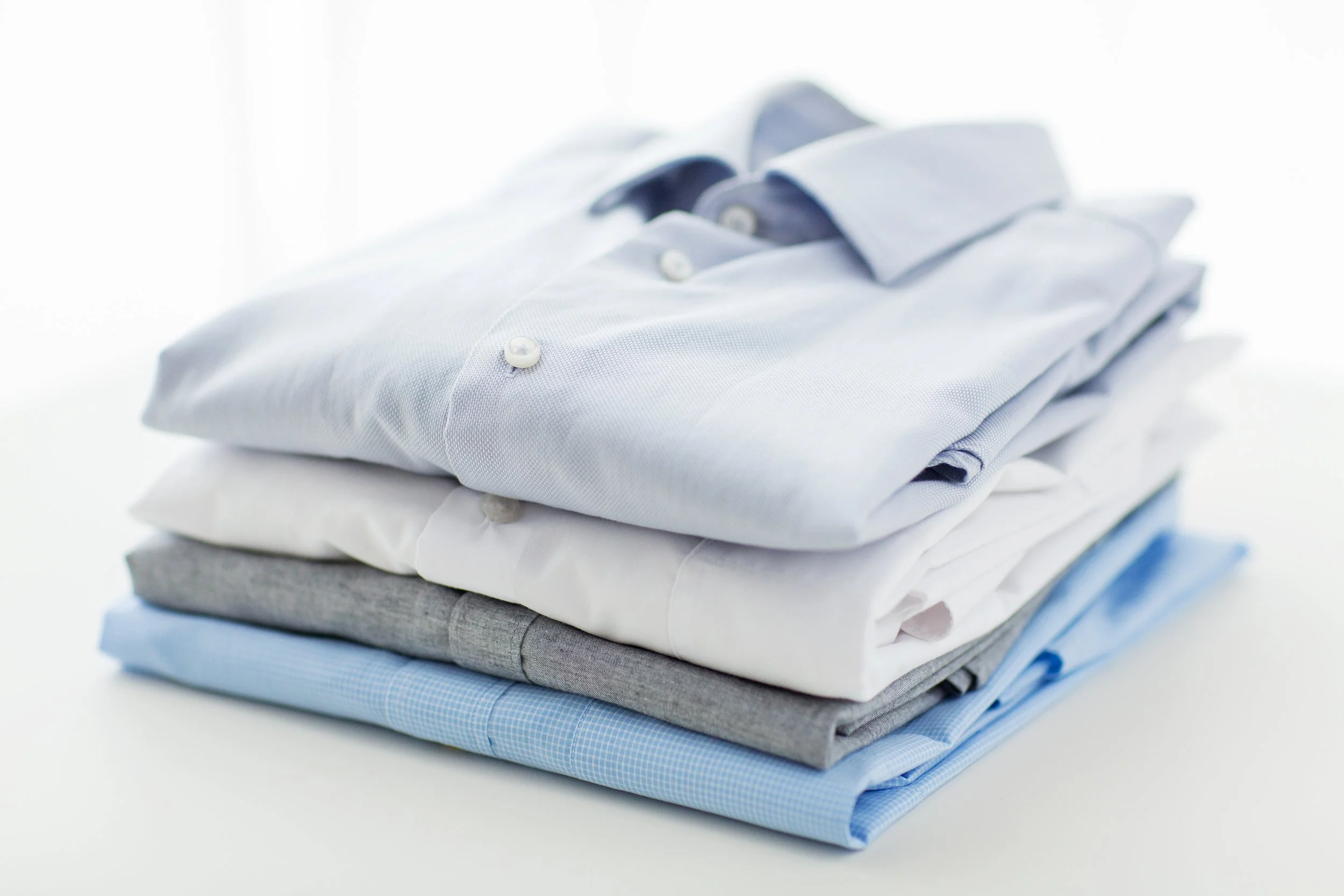 Stack of folded dress shirts in various shades of blue, white, and gray