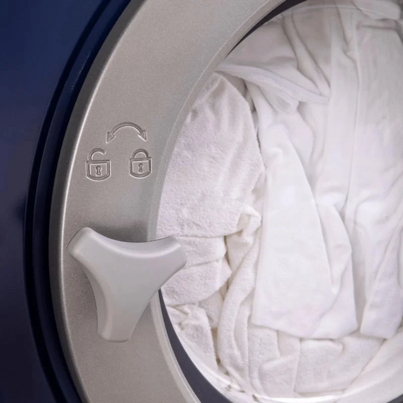 Front loading washing machine with white towels inside it.