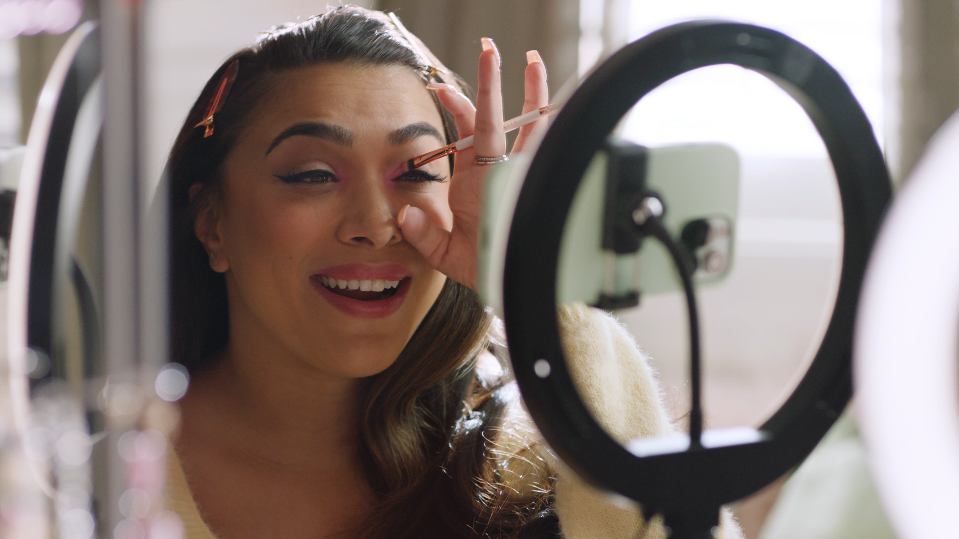 Woman applying makeup while filming a video with a ring light and smartphone.