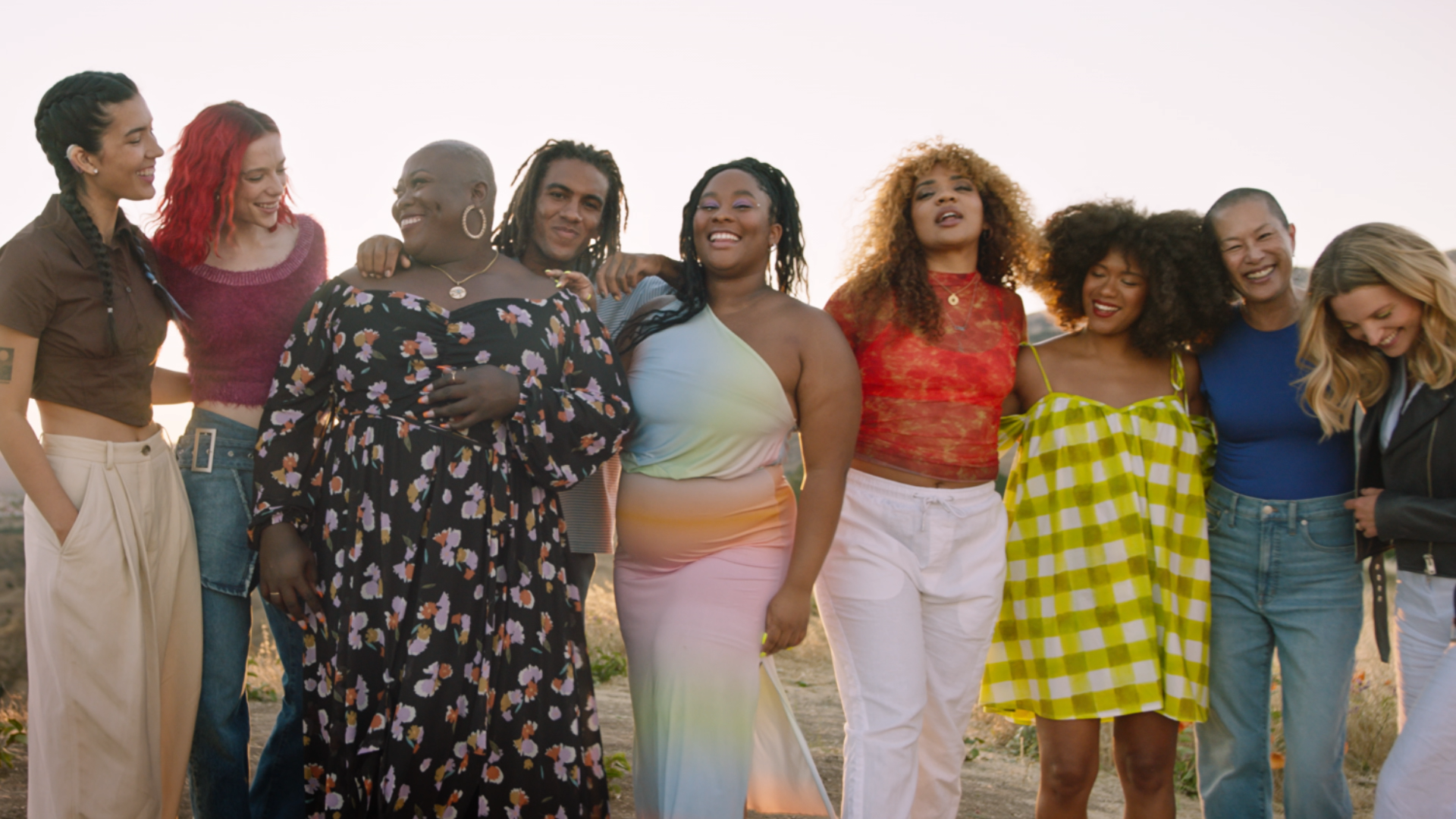 Group of diverse people in colorful clothing standing outdoors at sunset, smiling and happy.