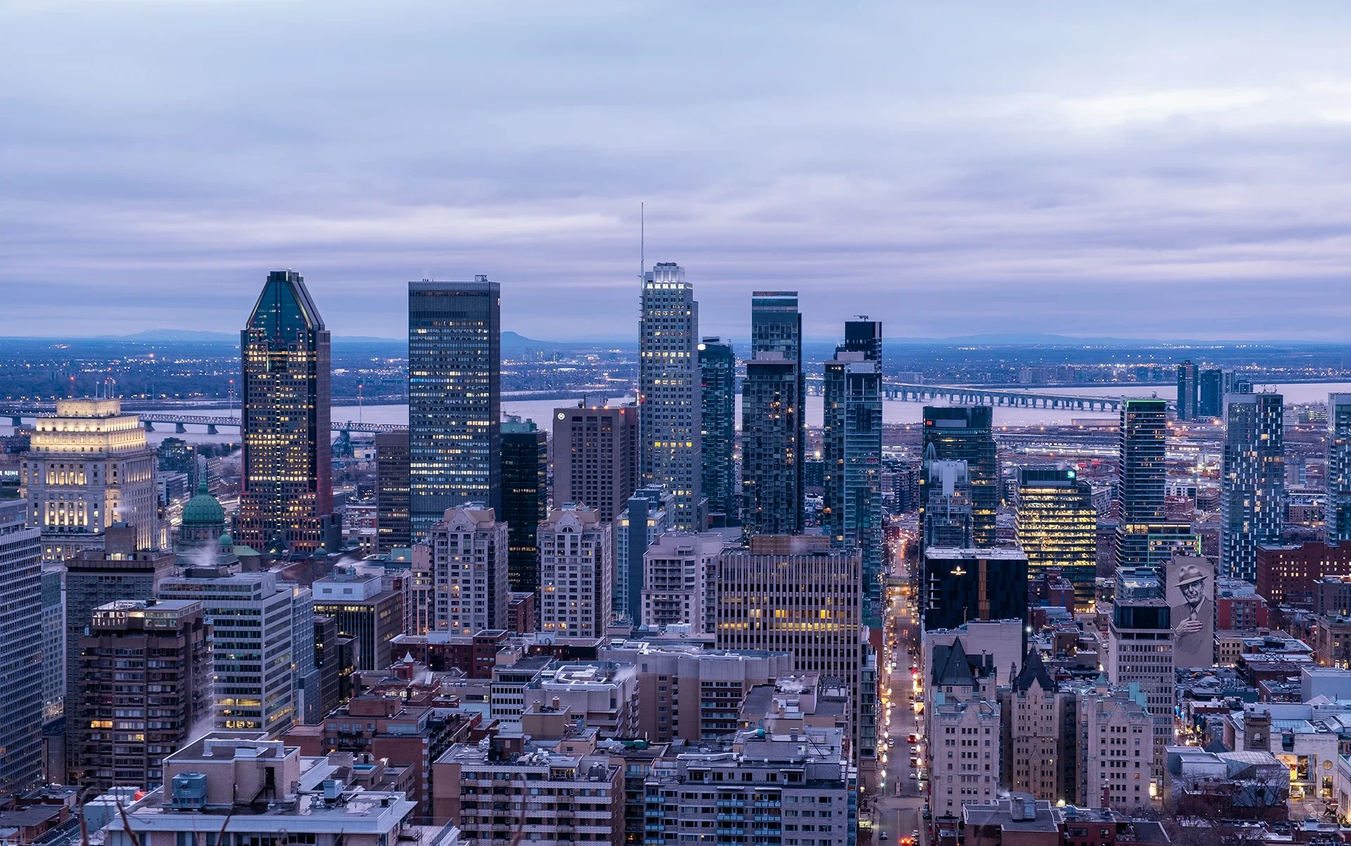 City skyline with tall skyscrapers during dusk, with a river and bridges in the background.