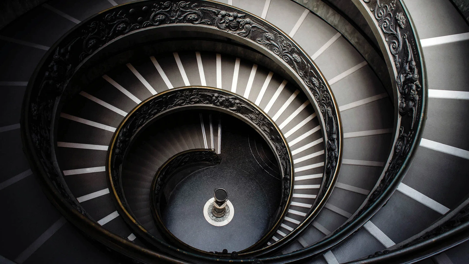 A top-down view of a spiral staircase with ornate black railings and gray steps.