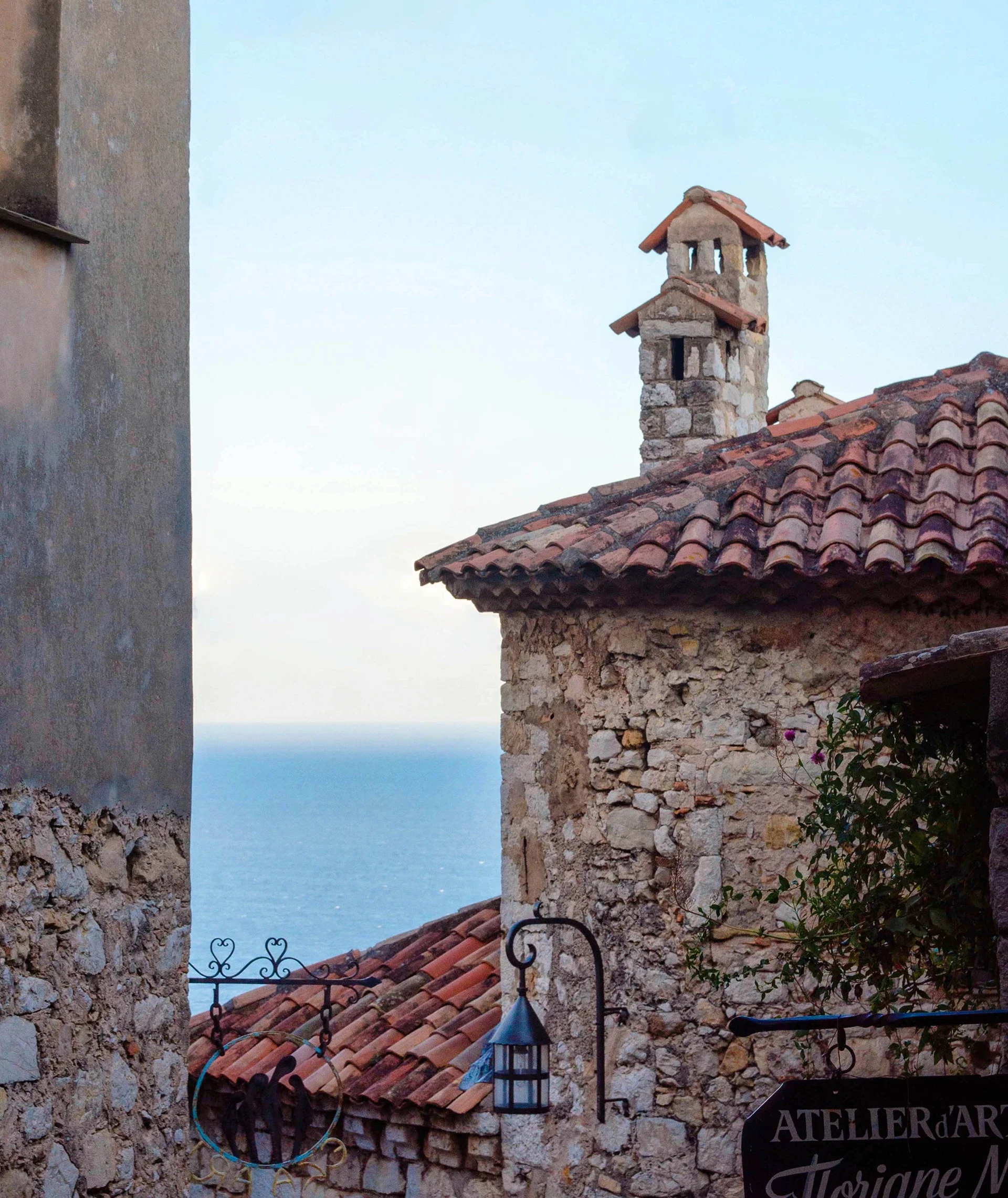 A view of rustic stone buildings with tiled roofs, overlooking the sea in the background.