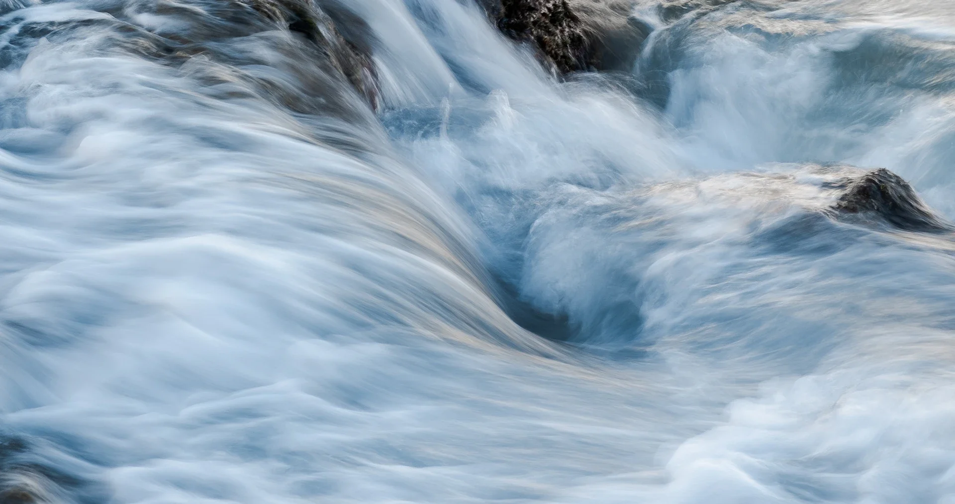 Moving ocean water with white foam and dark rocks beneath the surface.