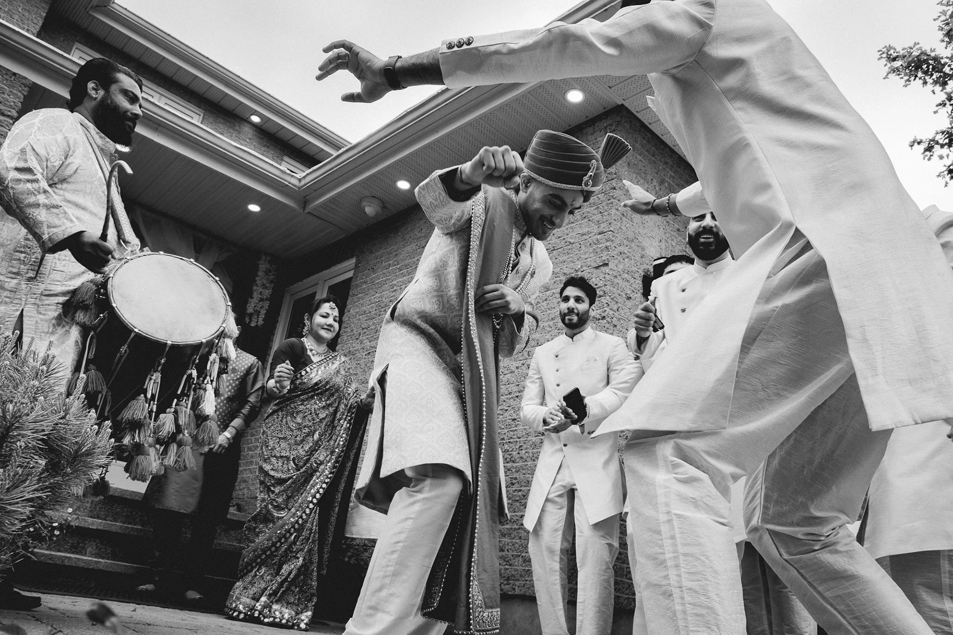 People celebrating at a wedding, dancing and playing instruments outside a house.