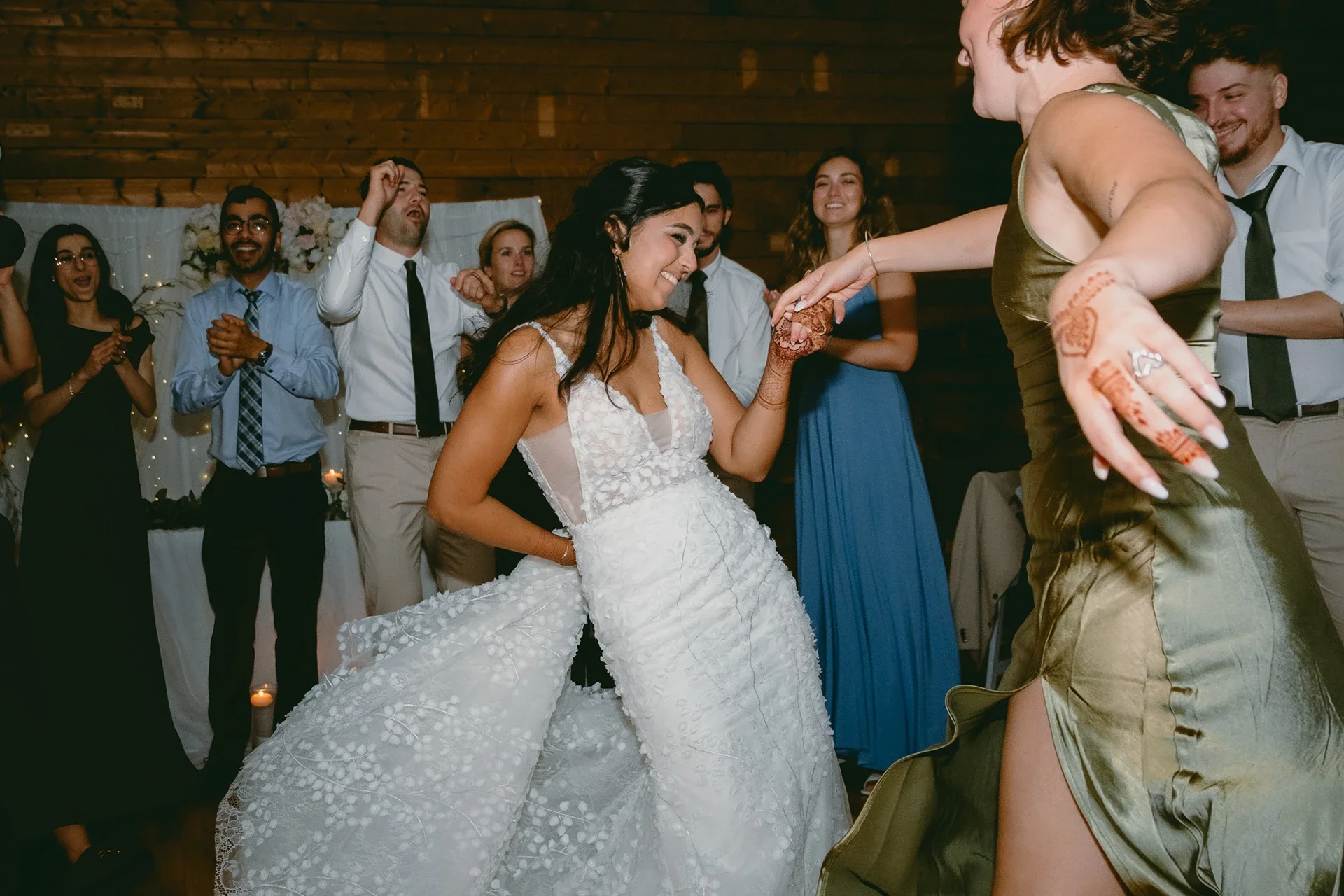 Bride and guest dancing at a wedding reception with guests clapping and smiling in the background.