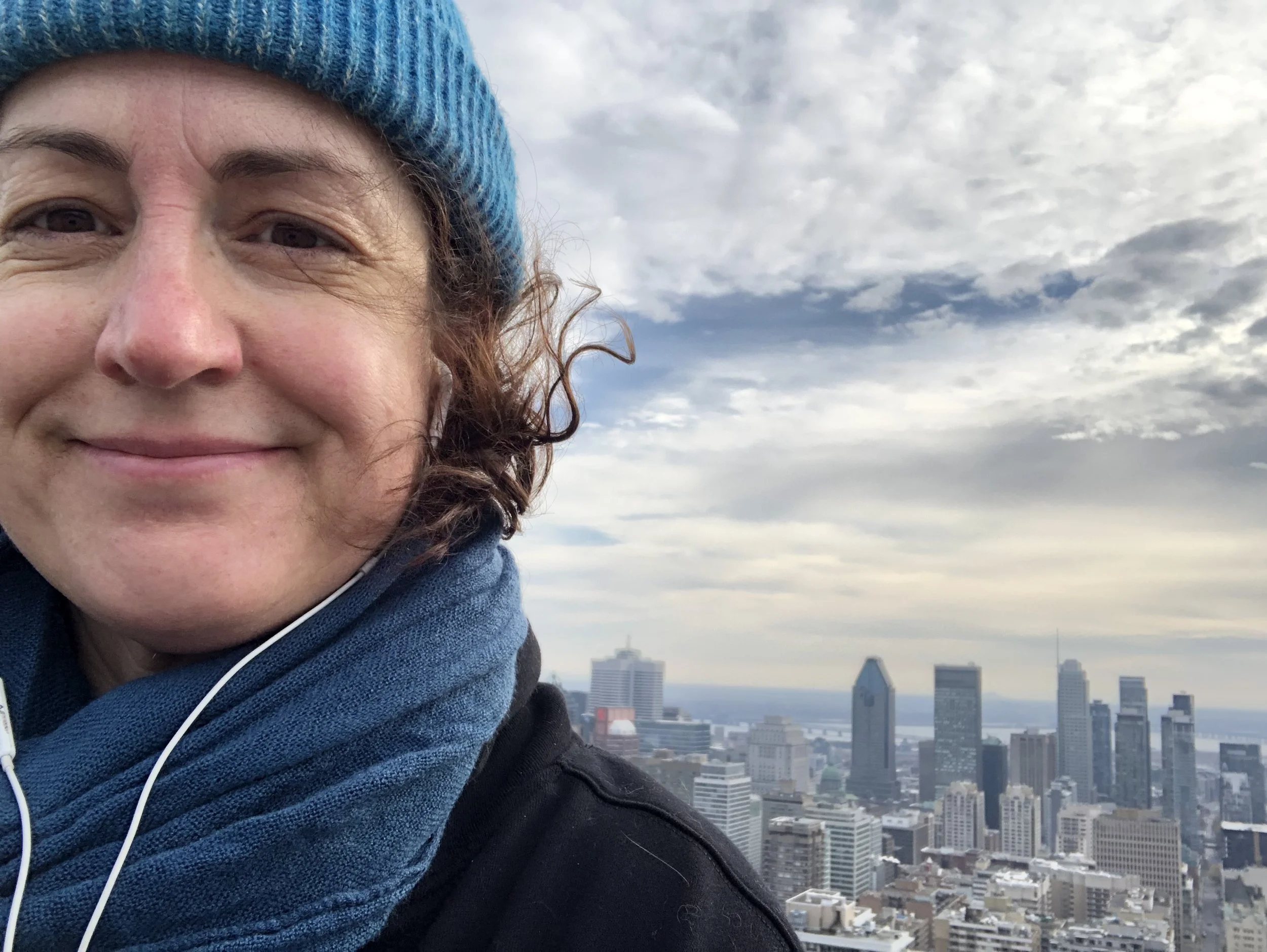 A person smiling with a city skyline and cloudy sky in the background.