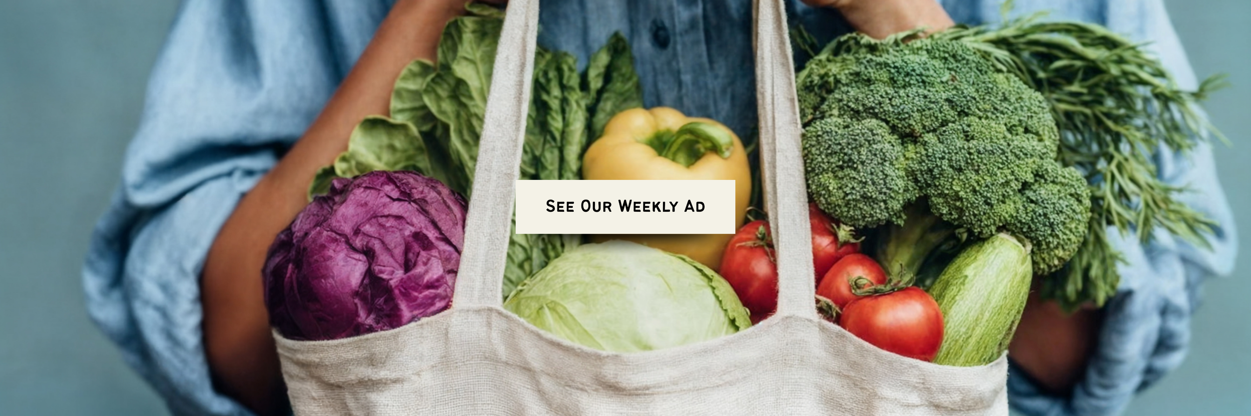 Person holding a fabric basket filled with fresh vegetables including purple cabbage, green lettuce, yellow bell pepper, broccoli, tomatoes, and zucchini, with a text overlay saying 'See Our Weekly Ad.'