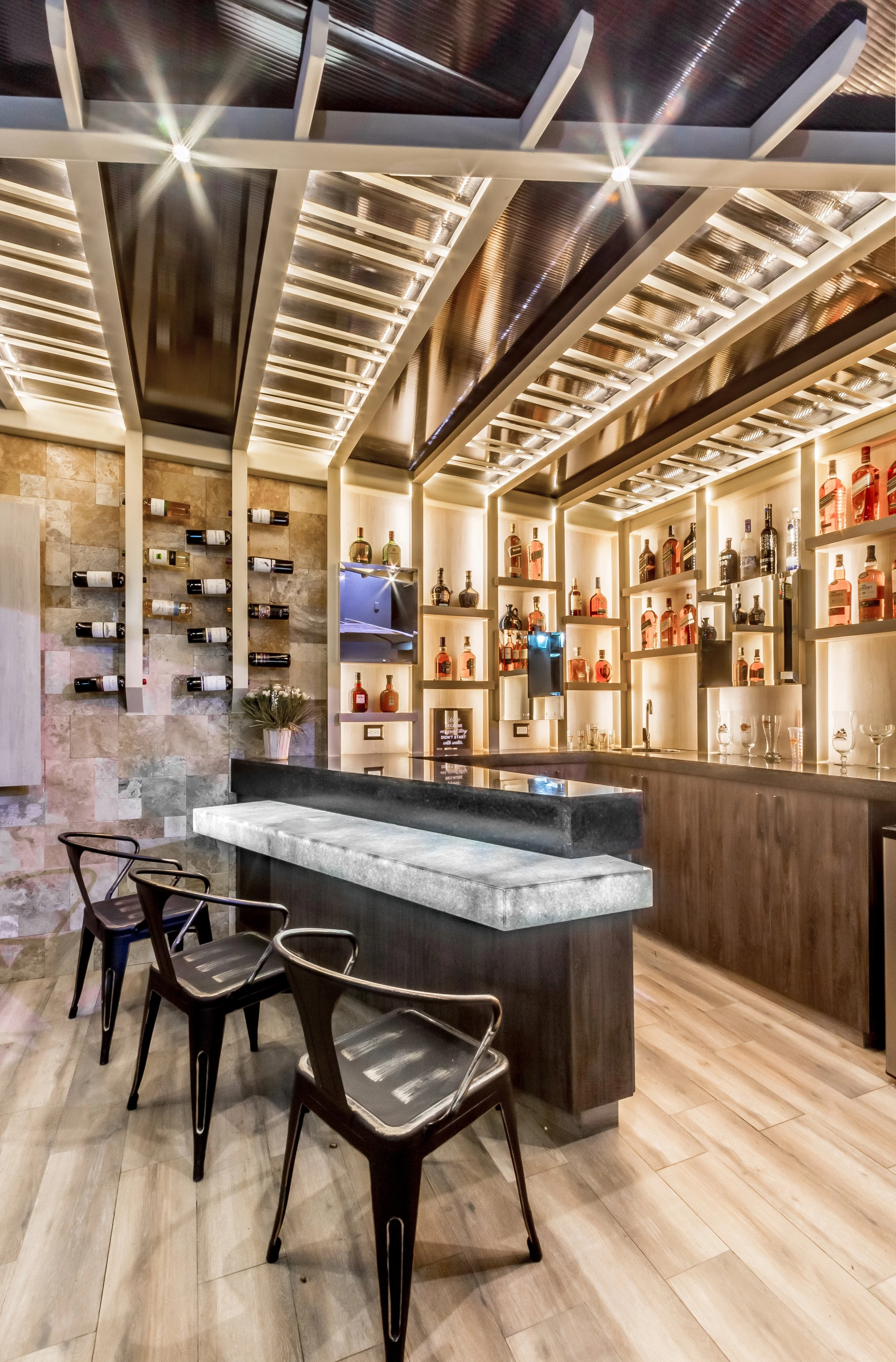 Bar moderna con estanterías con botellas de licor, cuatro sillas negras y un mostrador de mármol.