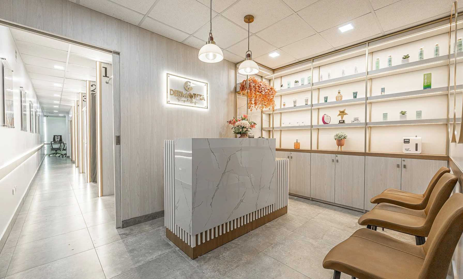 Vestíbulo de clínica con mostrador de mármol, estantería con productos, sillas de espera y decoración floral.