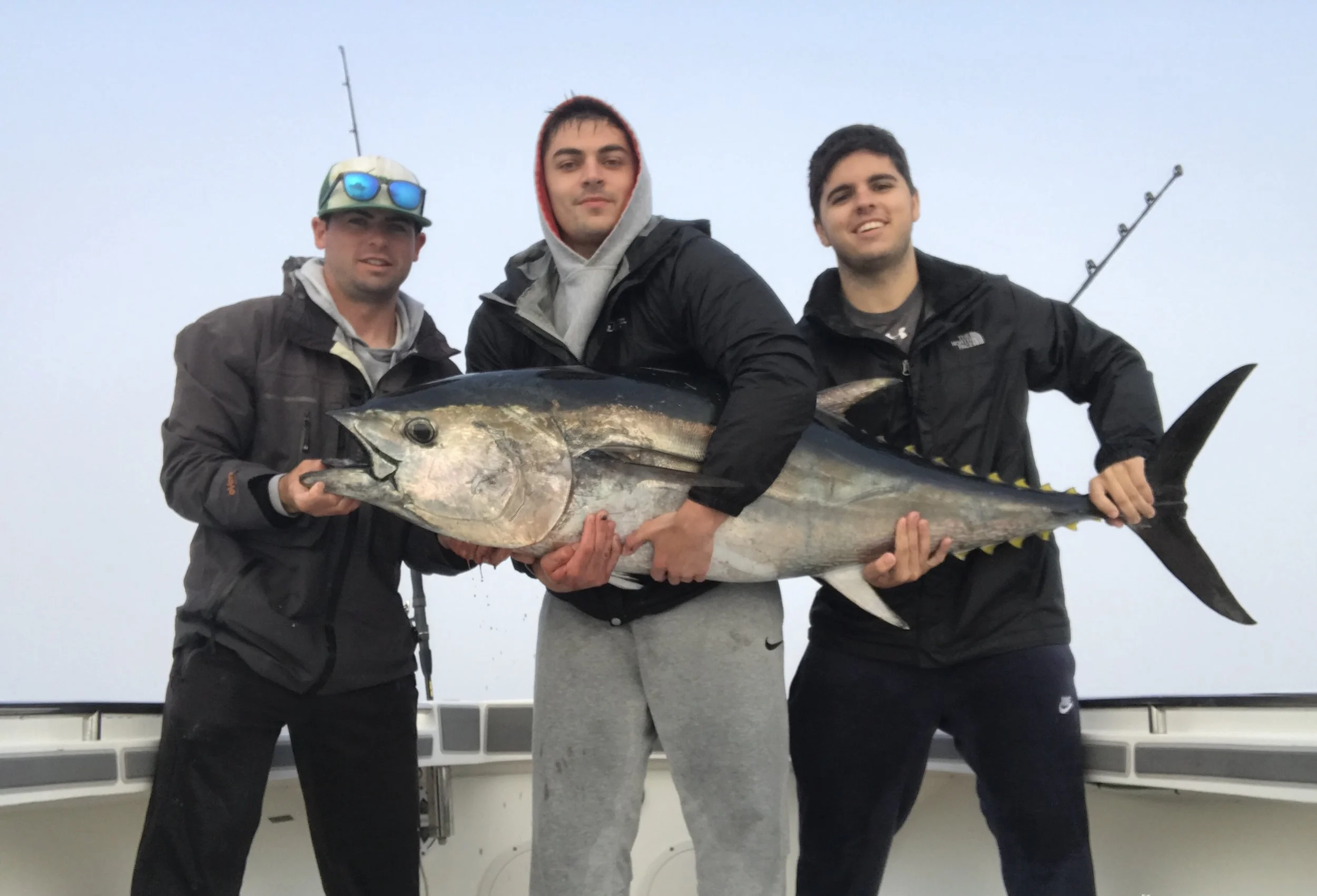 Three men on a boat holding a large tuna fish.