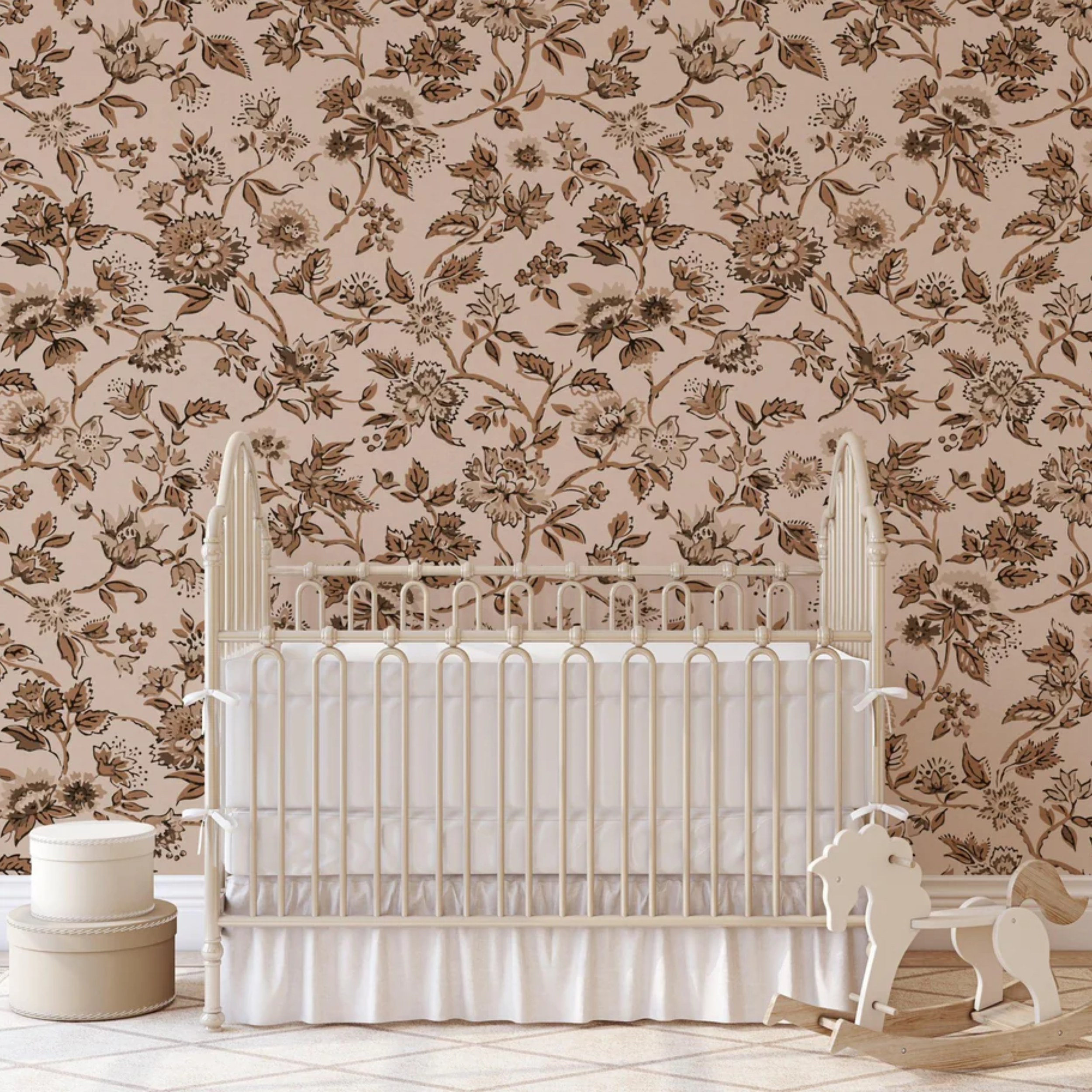 A white crib with a high back and spindled sides against a floral wallpapered wall with tan and brown flowers. To the left of the crib is a round, tiered white table with a white lamp on top, and to the right is a white rocking horse.