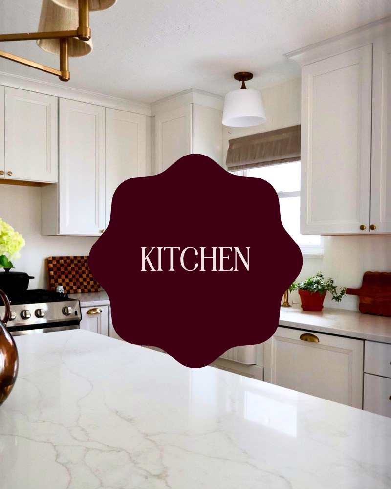 Bright kitchen with white cabinets, marble countertop, window with beige shade, potted plants, and a combination of brass and wooden accents.