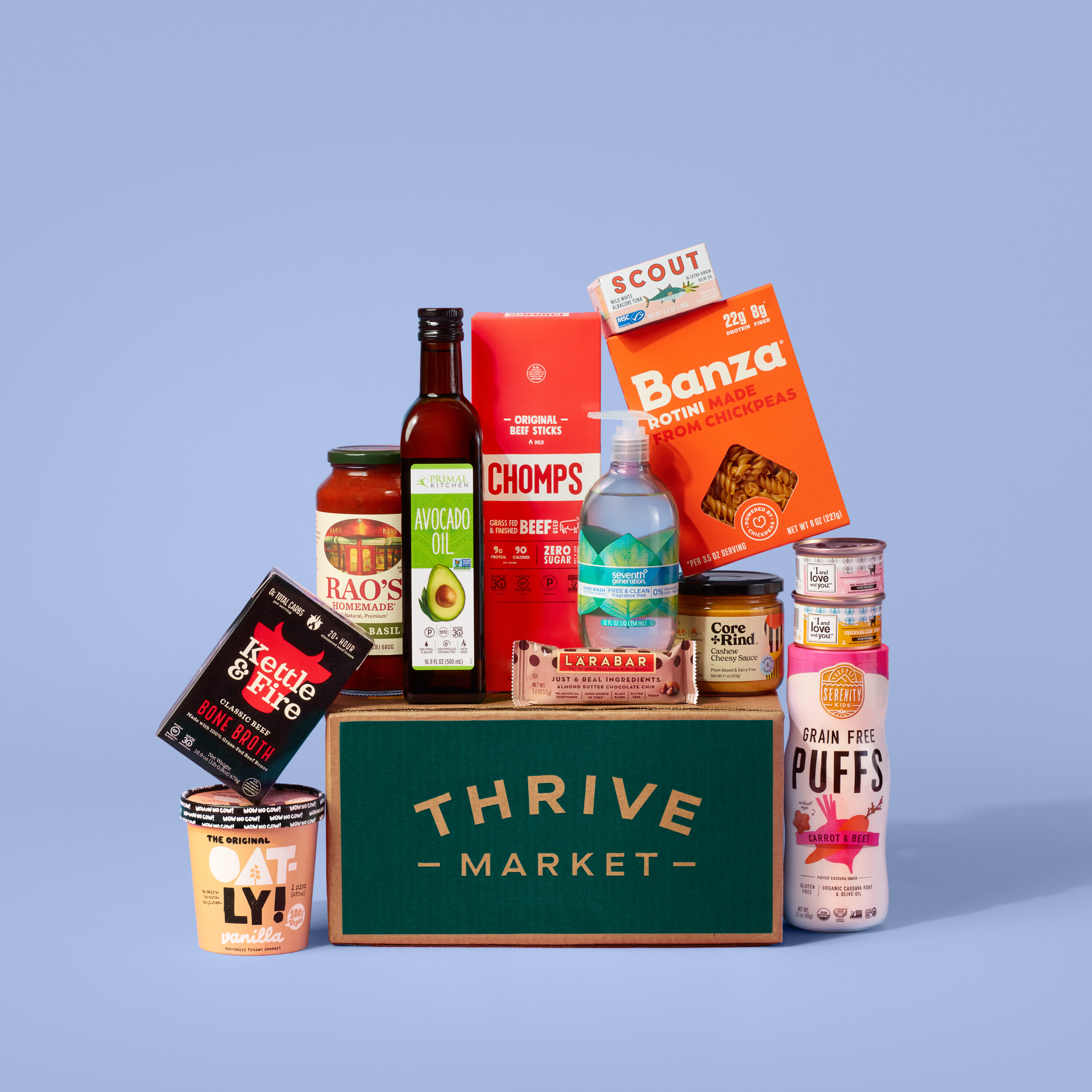 Various food products including a box of pasta, cans of chickpeas, tomato sauce, and jars of condiments on a green produce box with a blue background.