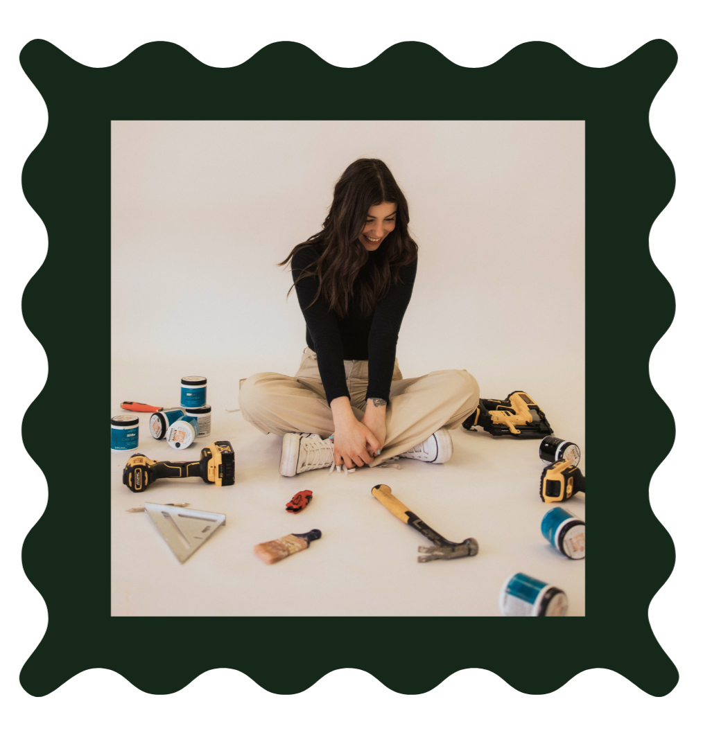 Kristen Ontiveros sitting on the floor surrounded by various tools and paint cans, smiling as she prepares for a DIY project.