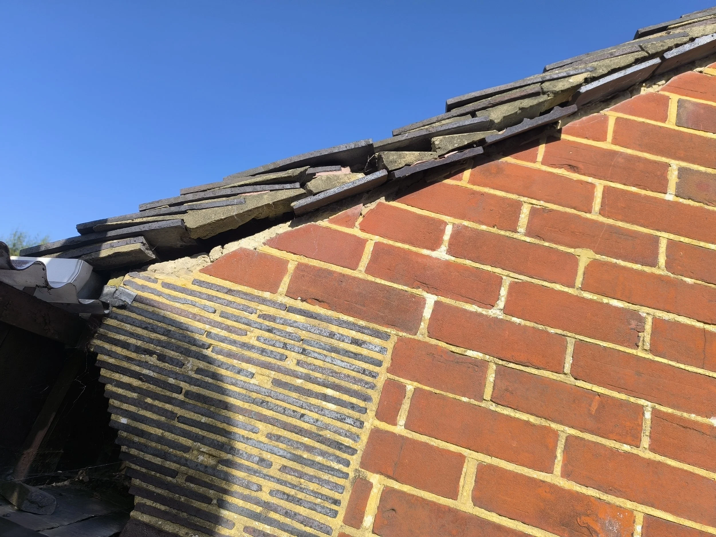 Close-up of a damaged brick chimney with different types of bricks and a clear blue sky in the background.