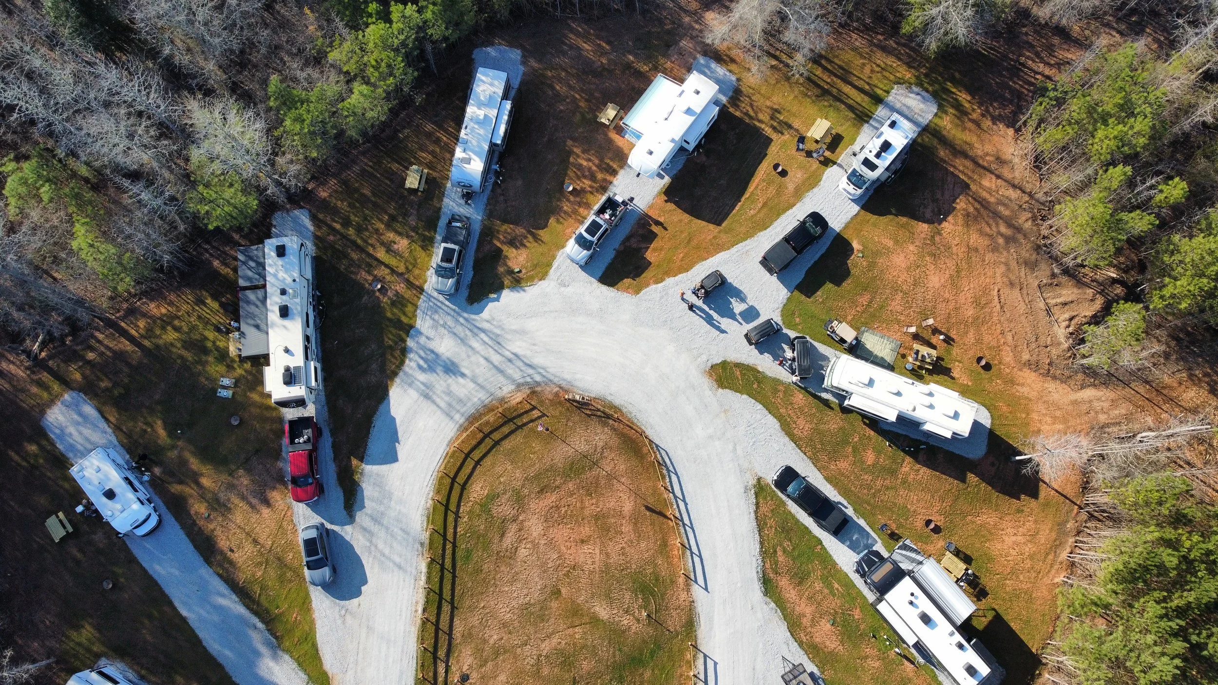 Aerial view of a campground with several RVs and vehicles parked on a gravel loop road, surrounded by trees.