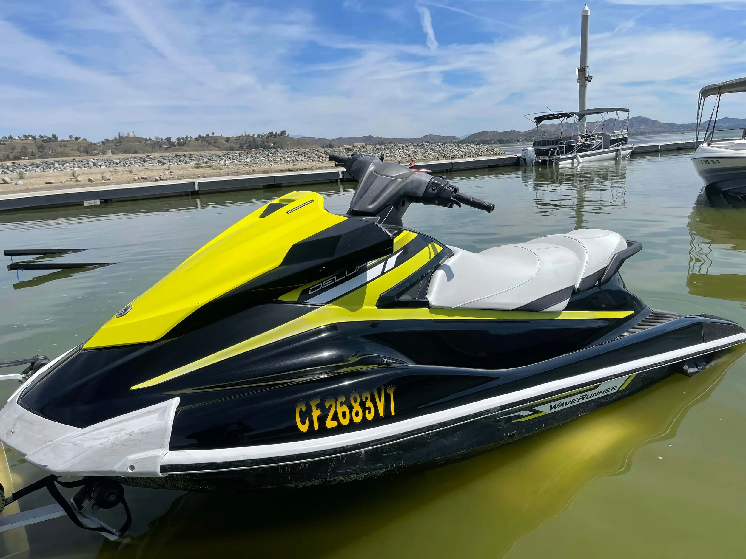 Yellow and black Yamaha WaveRunner jet ski docked at a marina with boats and hills in the background.