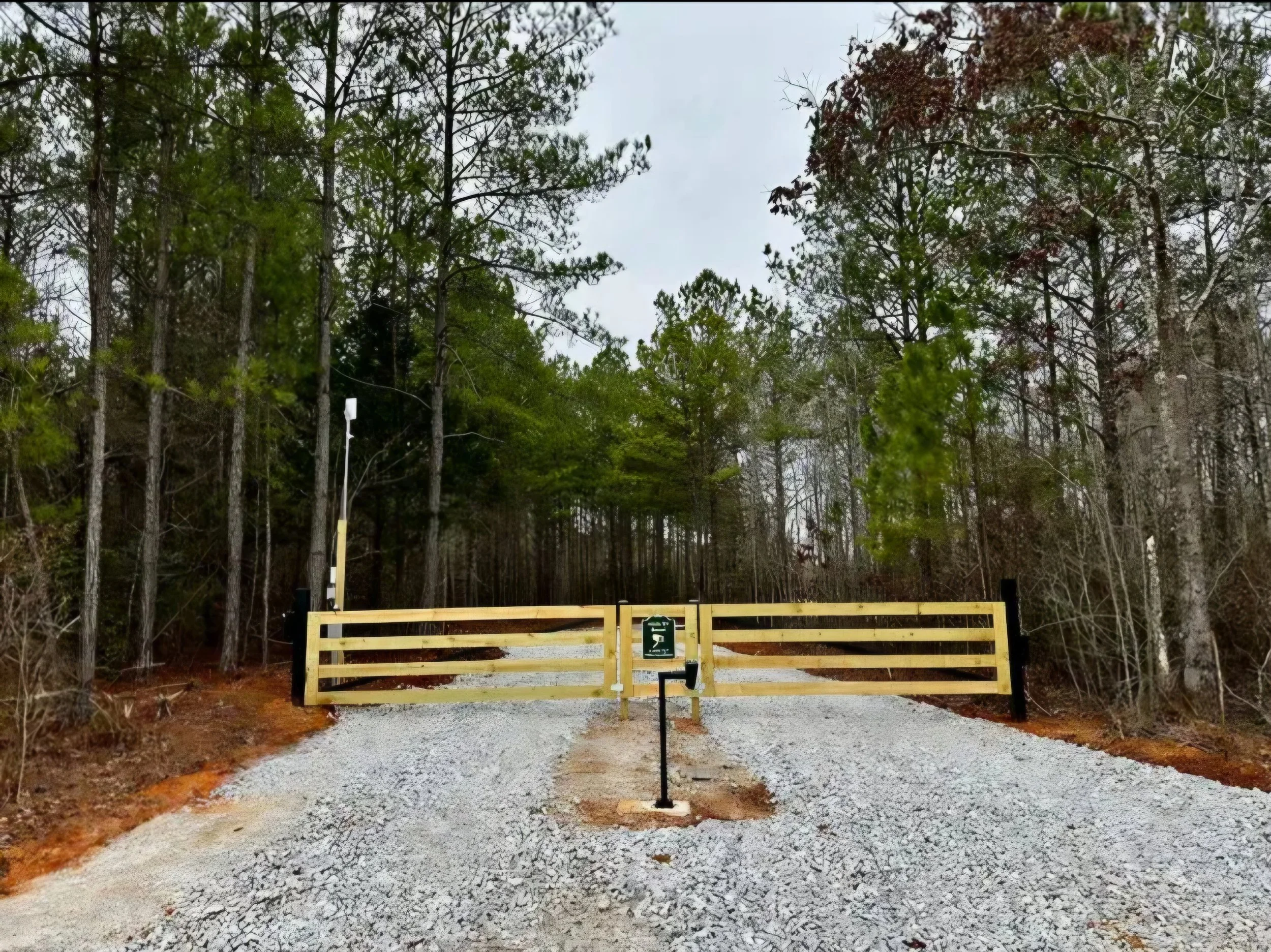 Wooden barrier gate across a gravel driveway giving secure access to a wooded campground around the bend, away from prying eyes.
