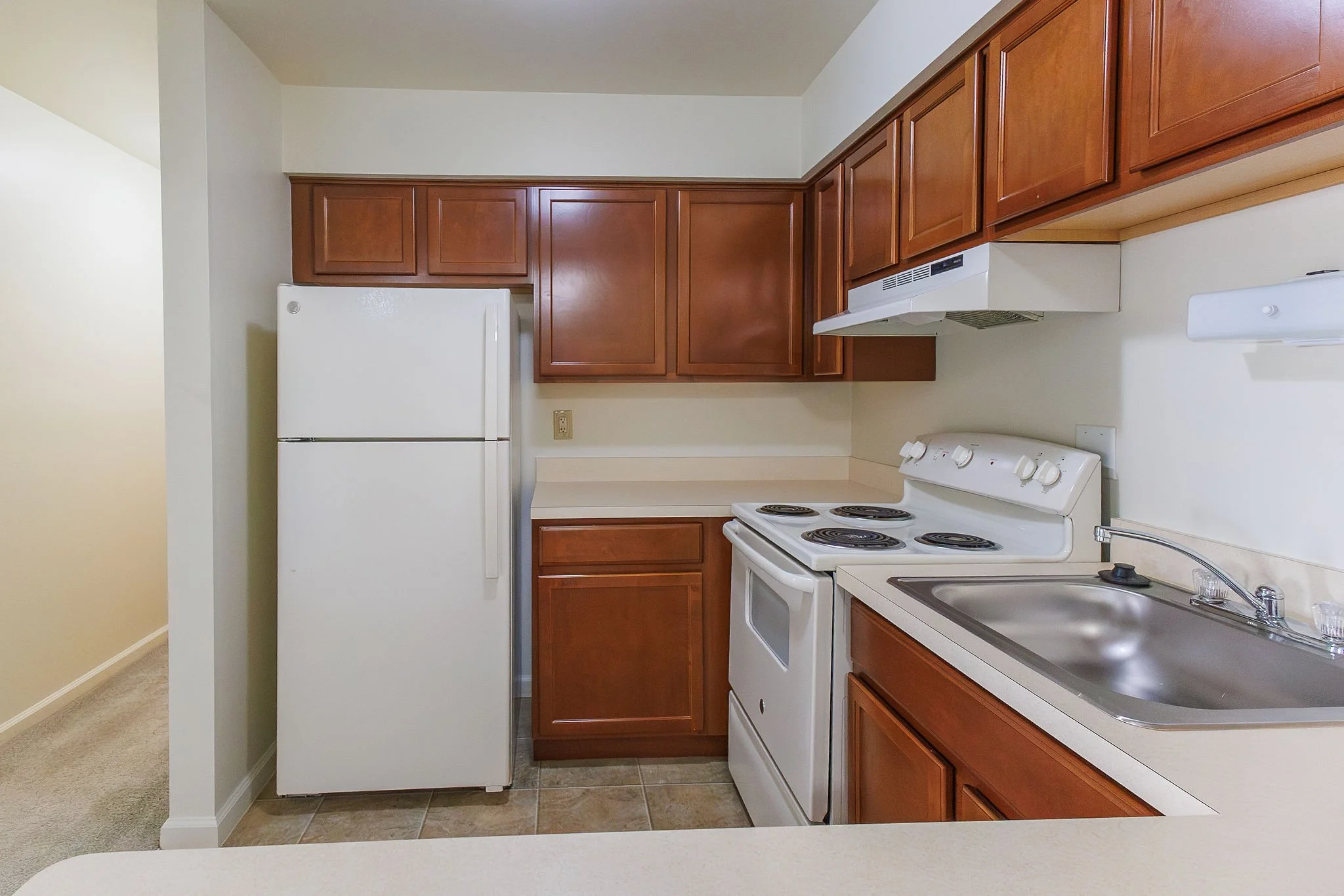 Kitchen with wooden cabinets, white refrigerator, oven with four burners, and sink with chrome faucet
