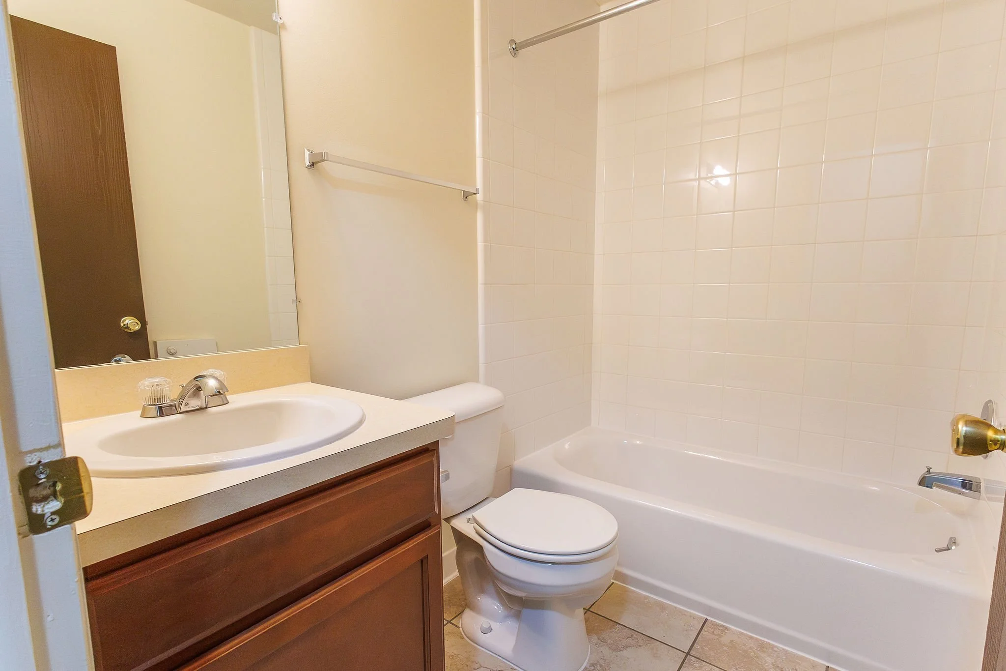 Bathroom featuring a wooden vanity with a white sink, a mirror, a toilet, and a bathtub with tiled wall surround.