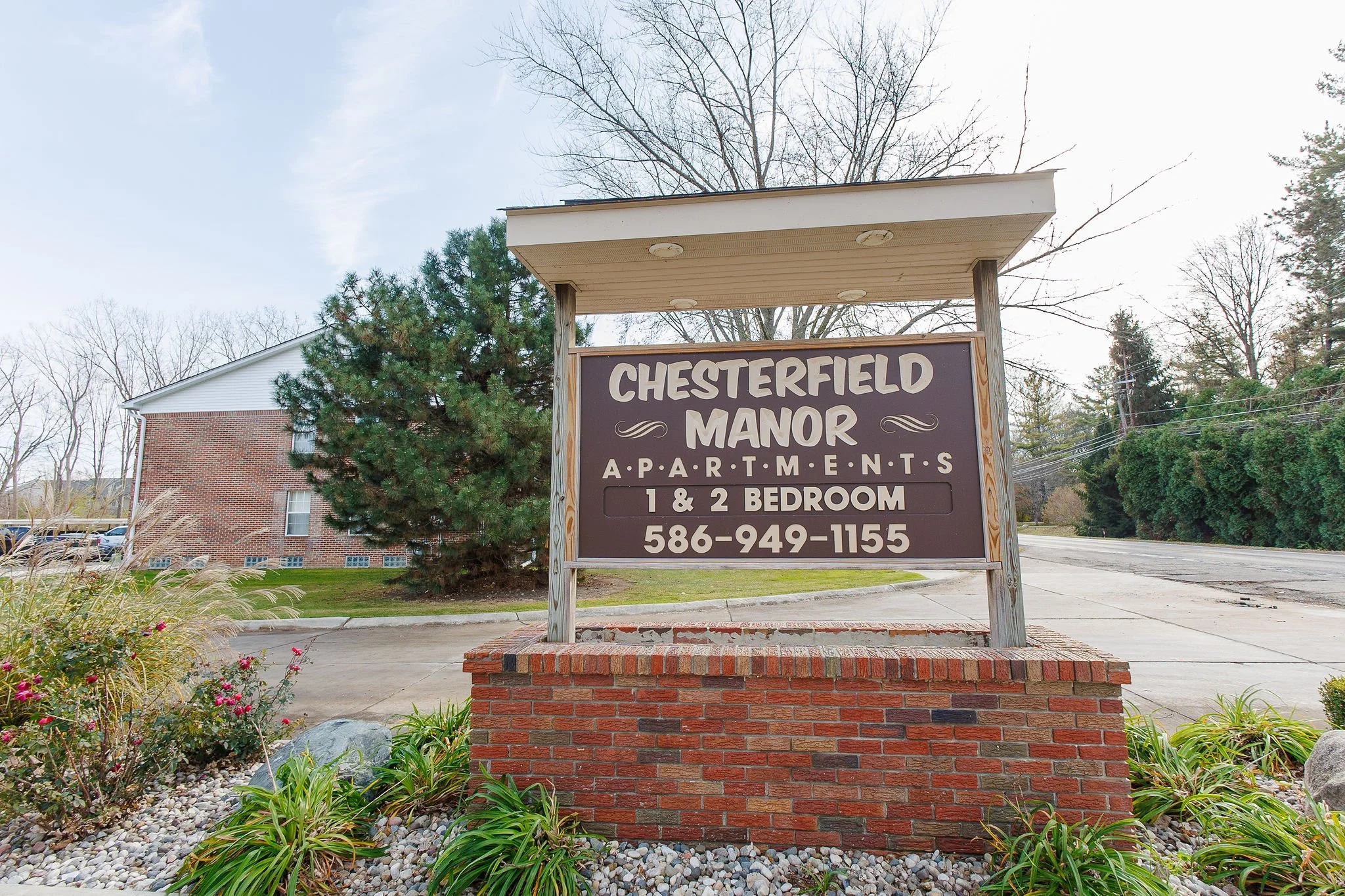 Sign for Chesterfield Manor Apartments for 1 and 2 bedroom units with a contact phone number, located outside on a brick base with surrounding greenery.