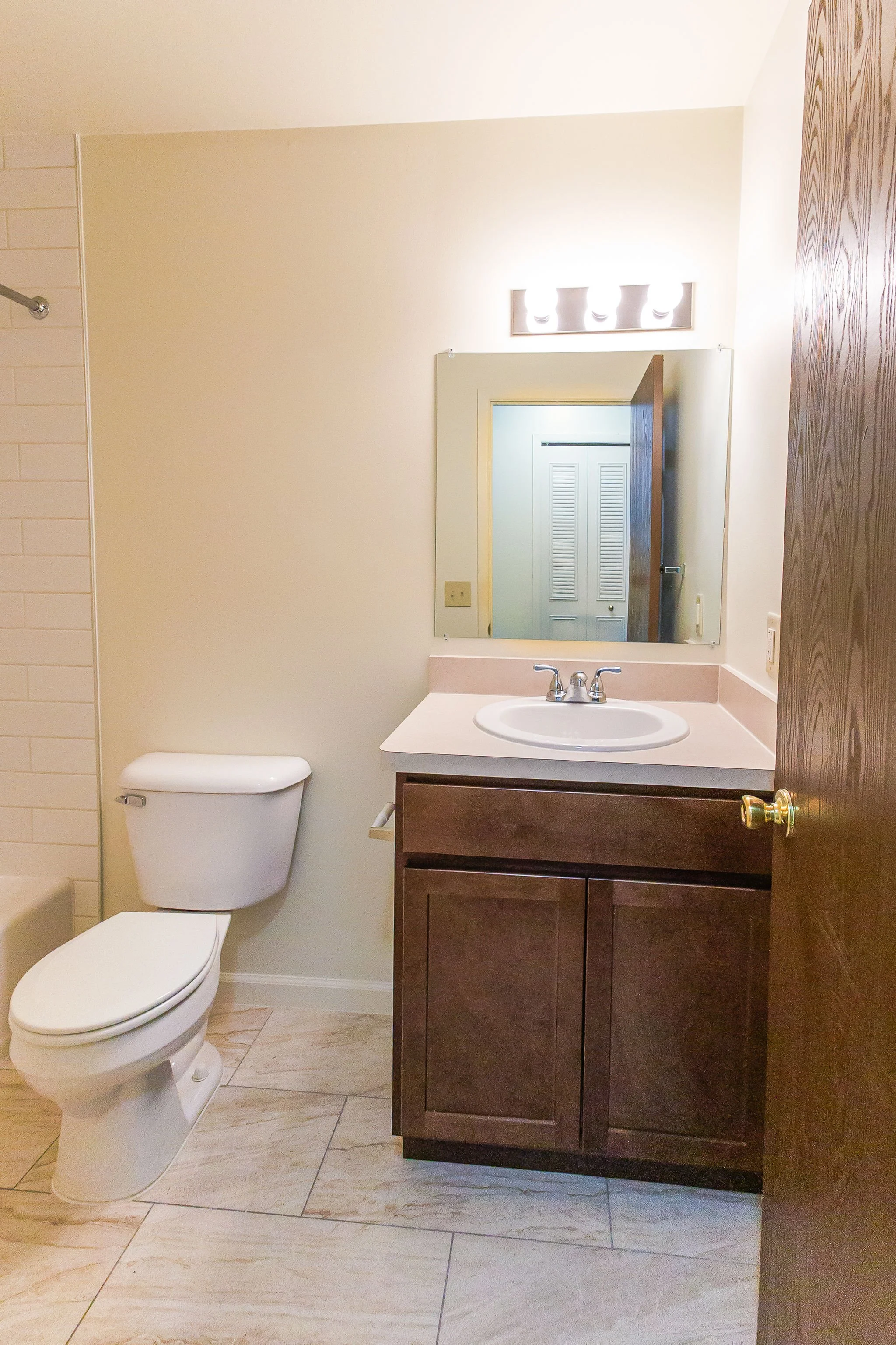 Bathroom with toilet, wooden vanity with sink, mirror, and light fixture above the mirror.