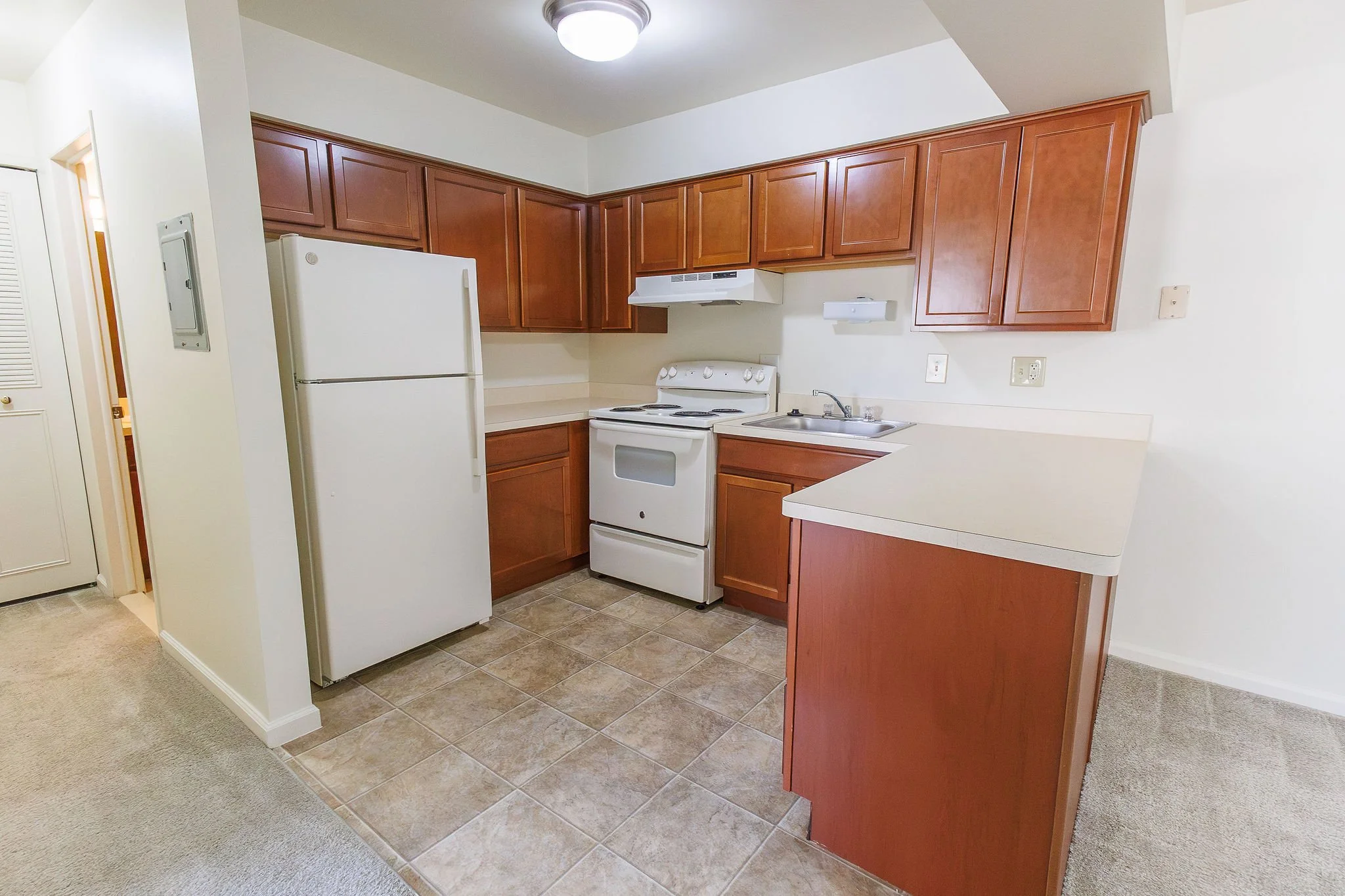 Kitchen with wood cabinets, white refrigerator, white electric stove, sink, and tiled floor.