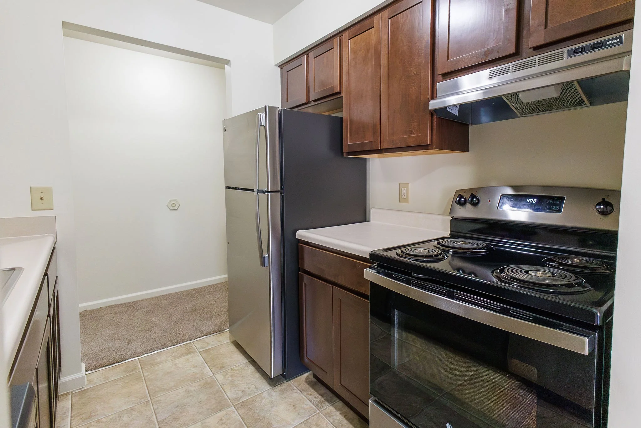 Kitchen with wooden cabinets, stainless steel refrigerator, black electric stove, and beige countertops.