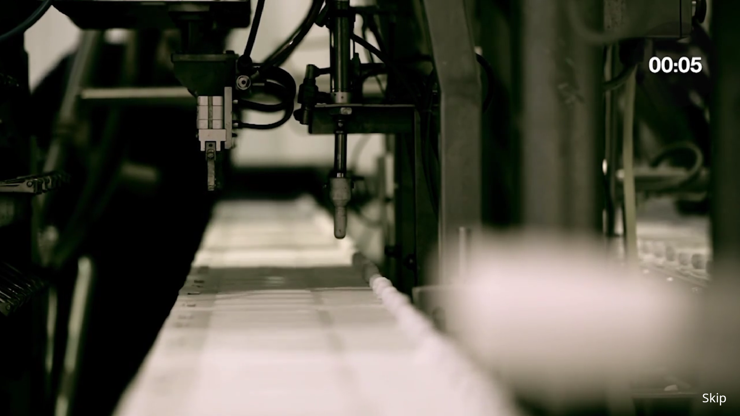 Close-up view of industrial machinery parts with mechanical arms, wires, and metal components in a factory or production setting.