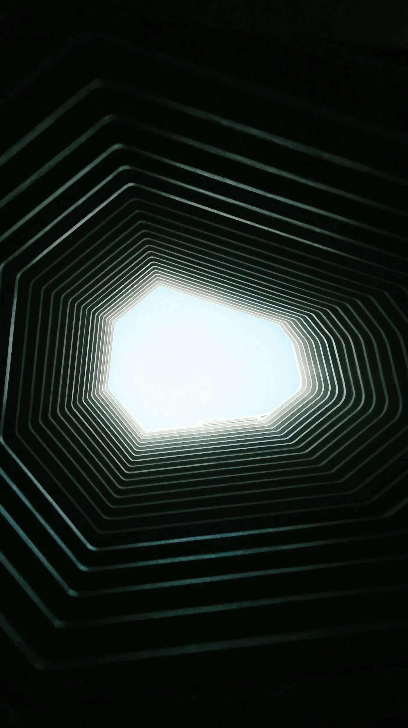 Vista de dentro de um edifício com estrutura vazada em forma de octógono, olhando para o céu