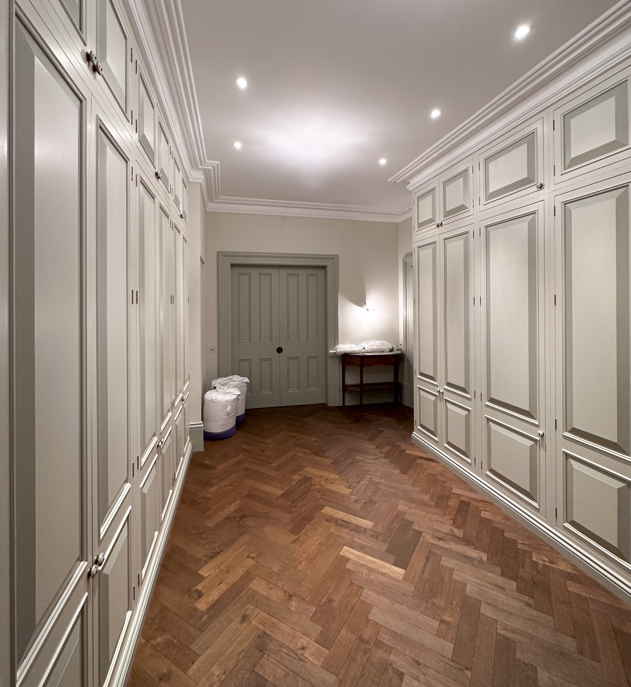 Empty walk-in closet with white built-in cabinets, wooden flooring, and ceiling lights.