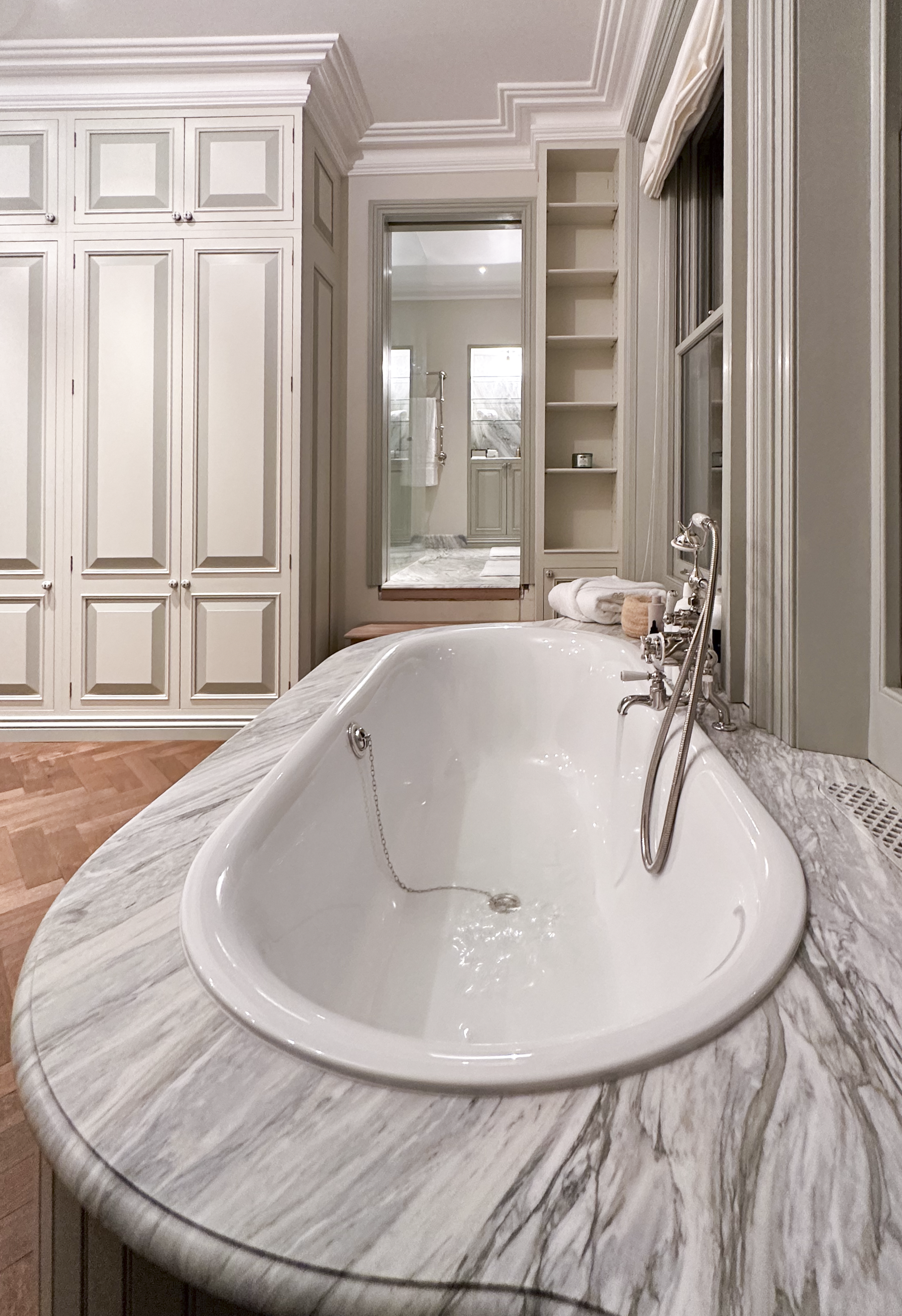 A luxurious bathroom featuring a large, oval-shaped bathtub with a marble surround, white cabinetry, and an adjacent walk-in shower visible through an open door.