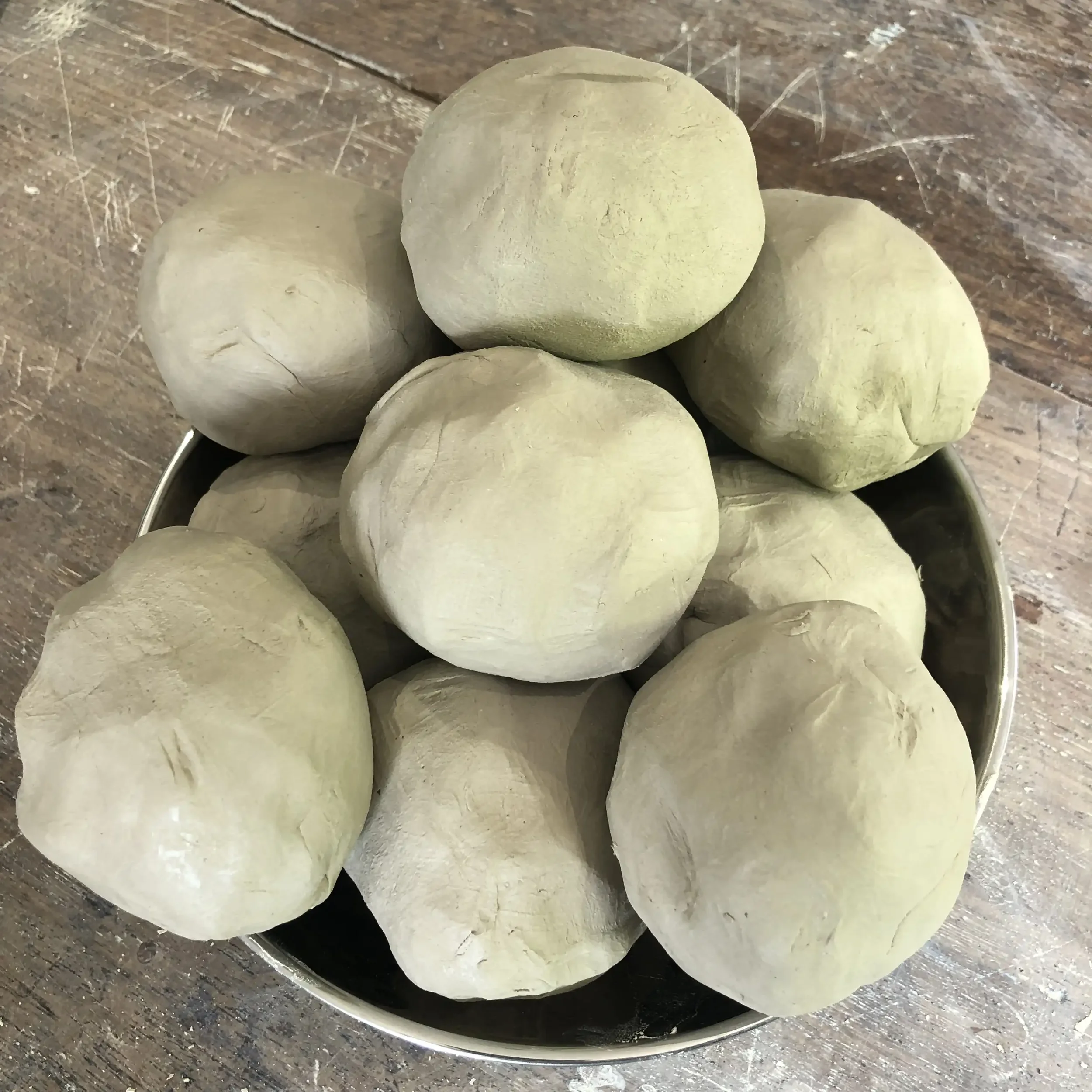 A bowl containing multiple balls of clay in a metal bowl on a wooden surface.
