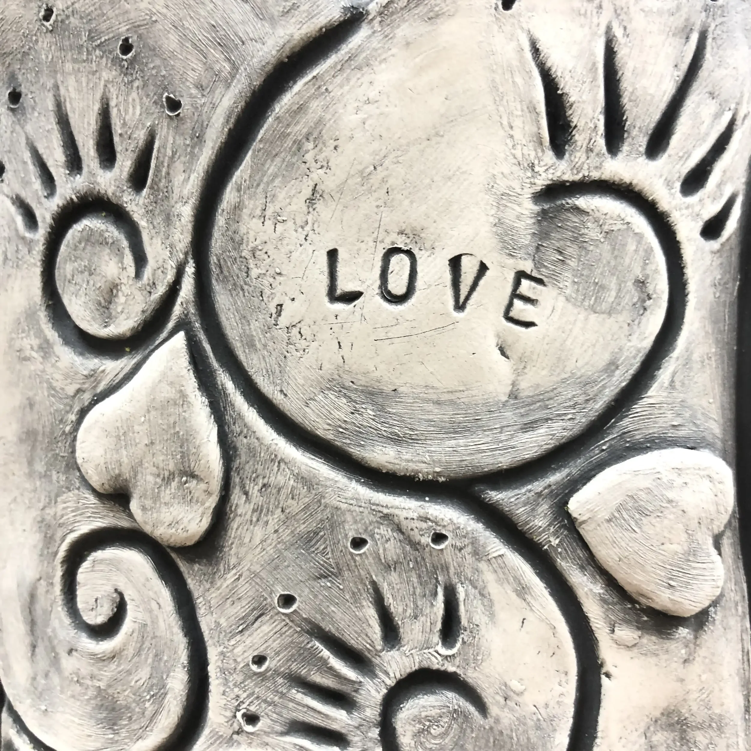 A textured clay post featuring hearts and swirls, with the word "LOVE" stamped into a central swirl shape.