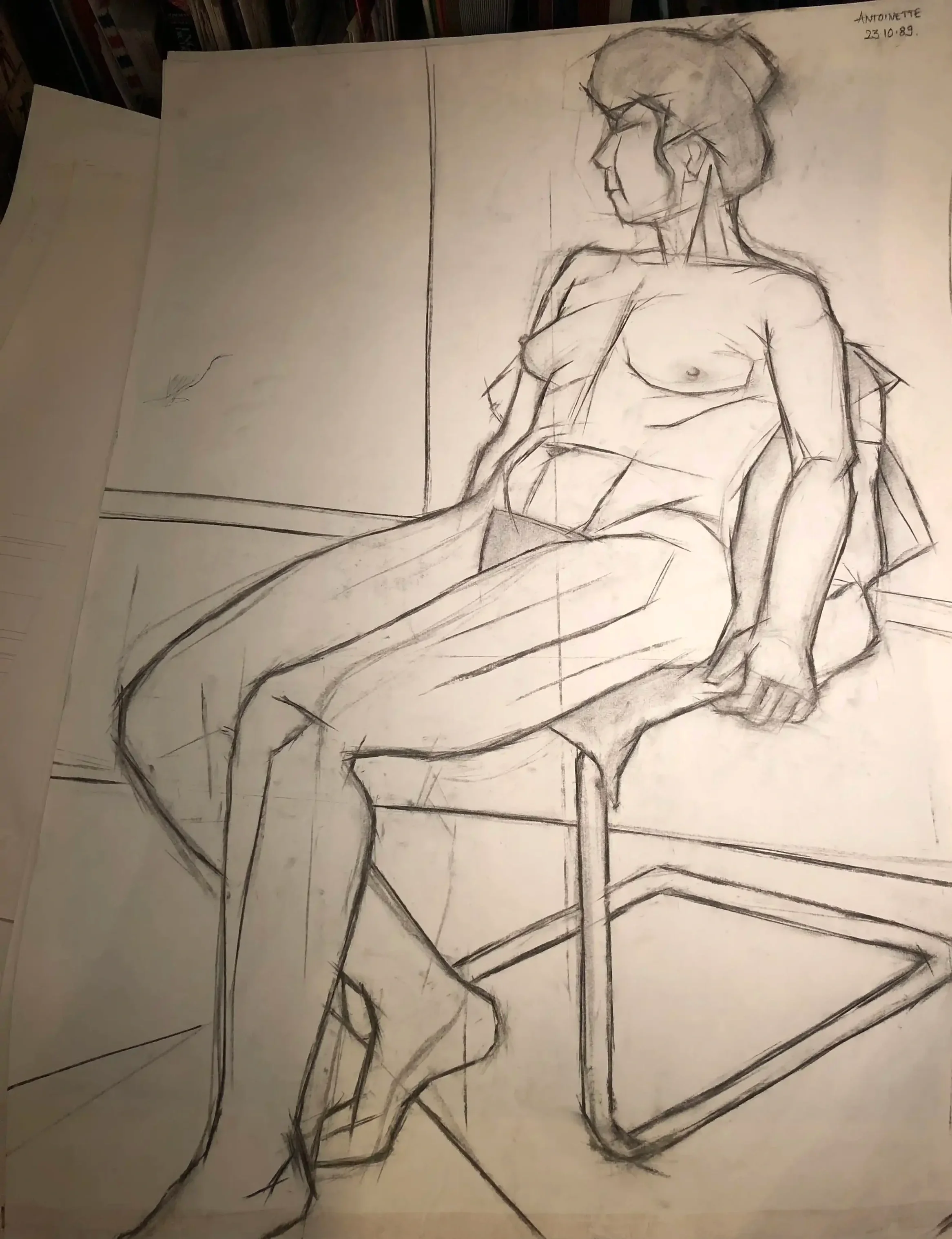 Sketch of a reclining nude woman sitting on a chair, with her hair tied up, seen from the side, on paper that is clipped to a drawing board.