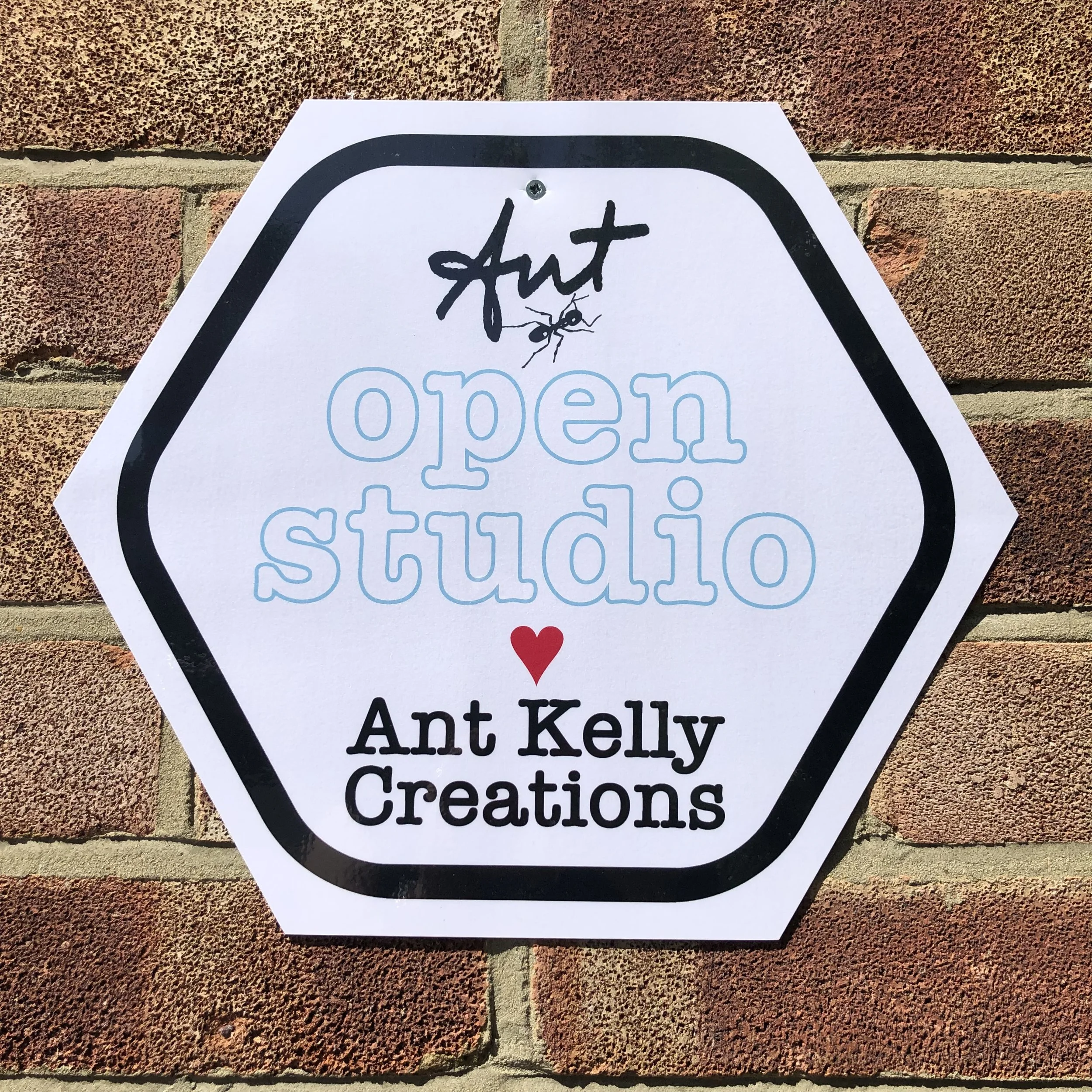 Sign on brick wall reads 'open studio' with a small ant graphic and the words 'Ant Kelly Creations' below, with a red heart symbol.