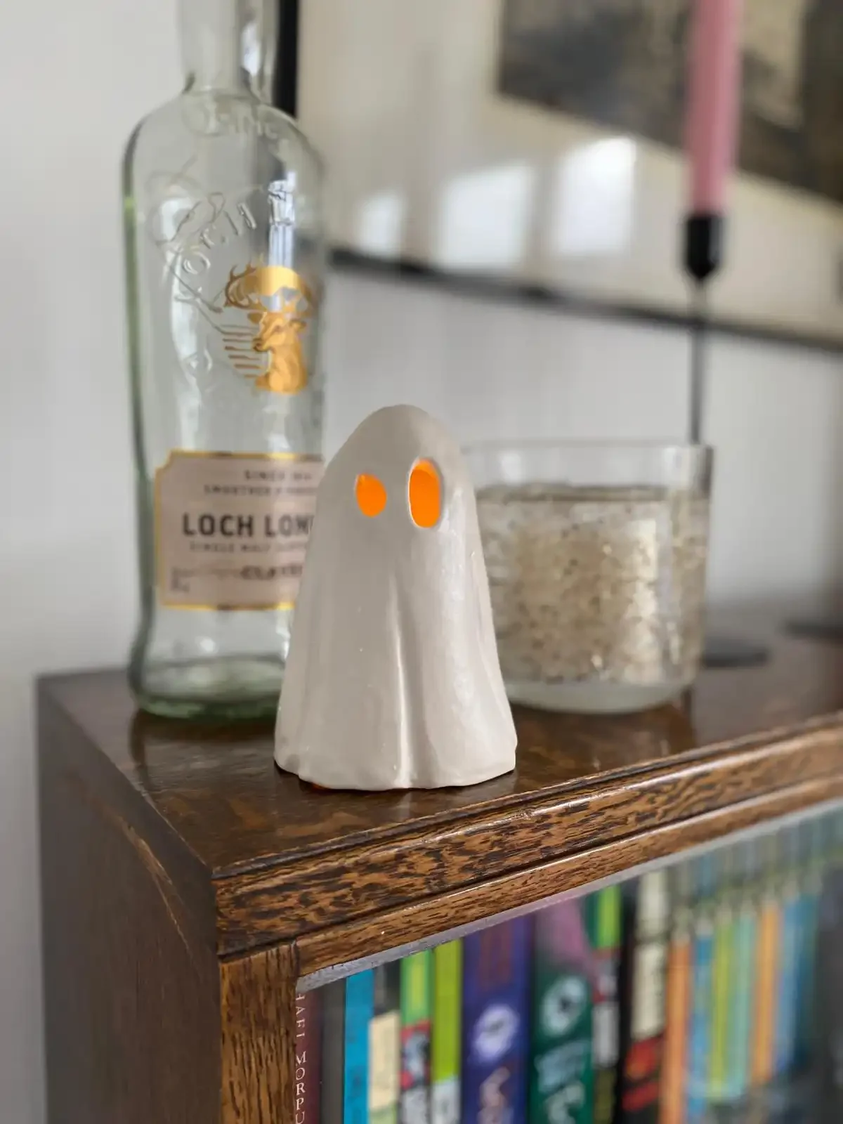 A small ghost-shaped ceramic figure with orange eyes on a wooden surface in a home setting.