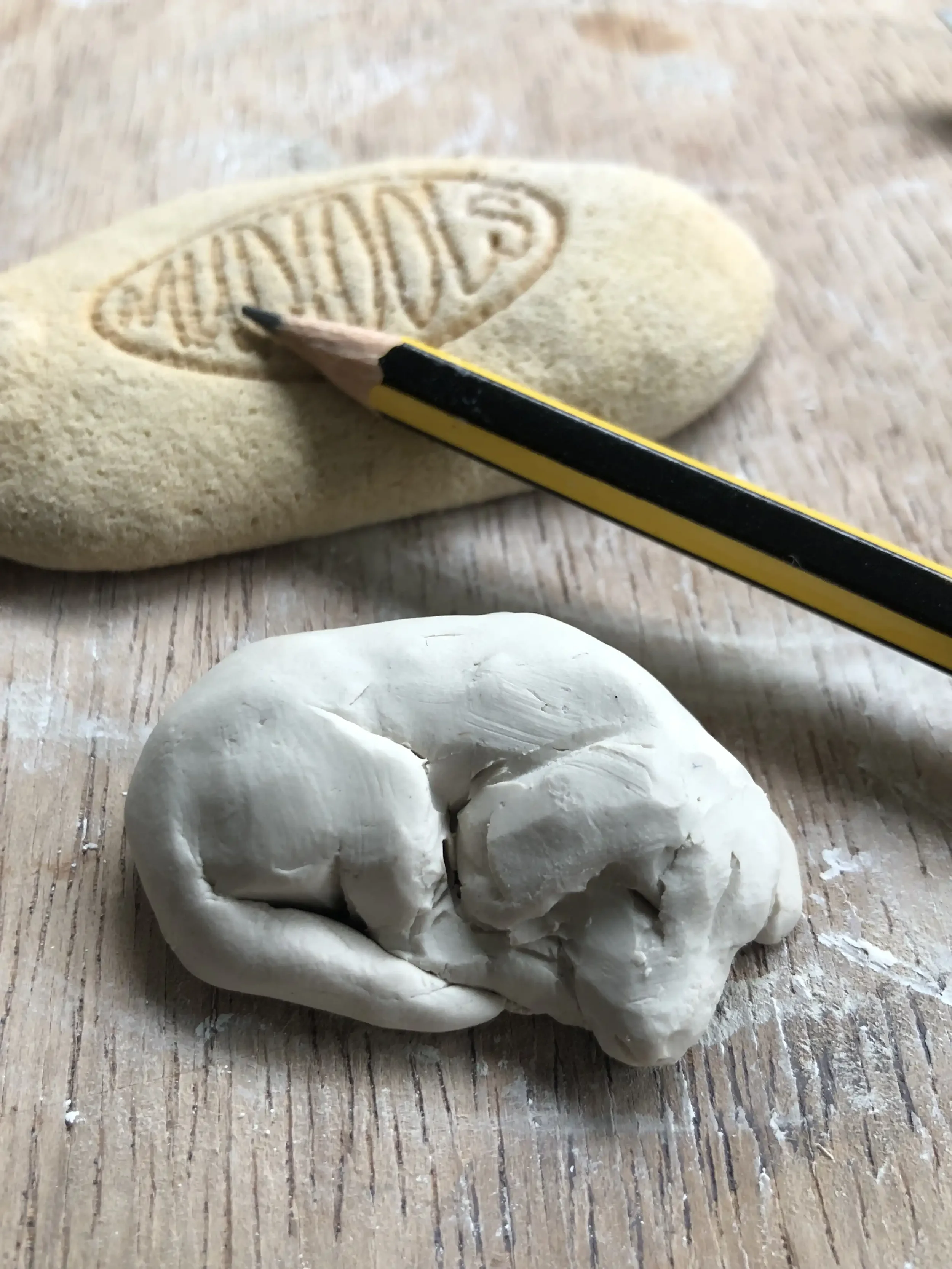 A small porcelain sculpture of a sleeping beagle sitting on a wooden surface, a flat sponge with the word 'MUDTOOLS' embossed into the surface, and a yellow and black pencil resting on the sponge.