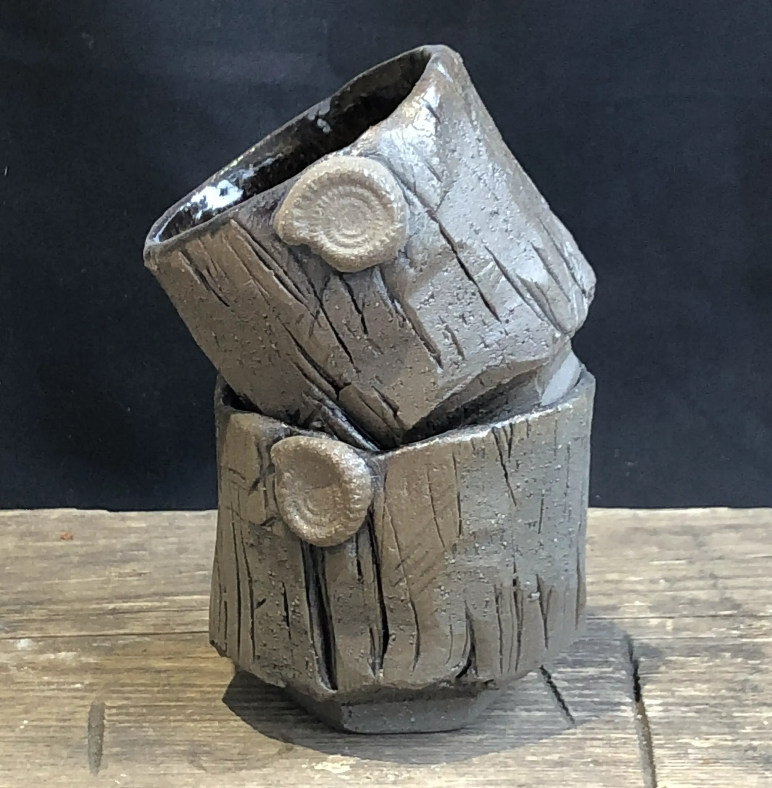 Two carved clay cups stacked on top of each other placed on a wooden surface against a dark background.