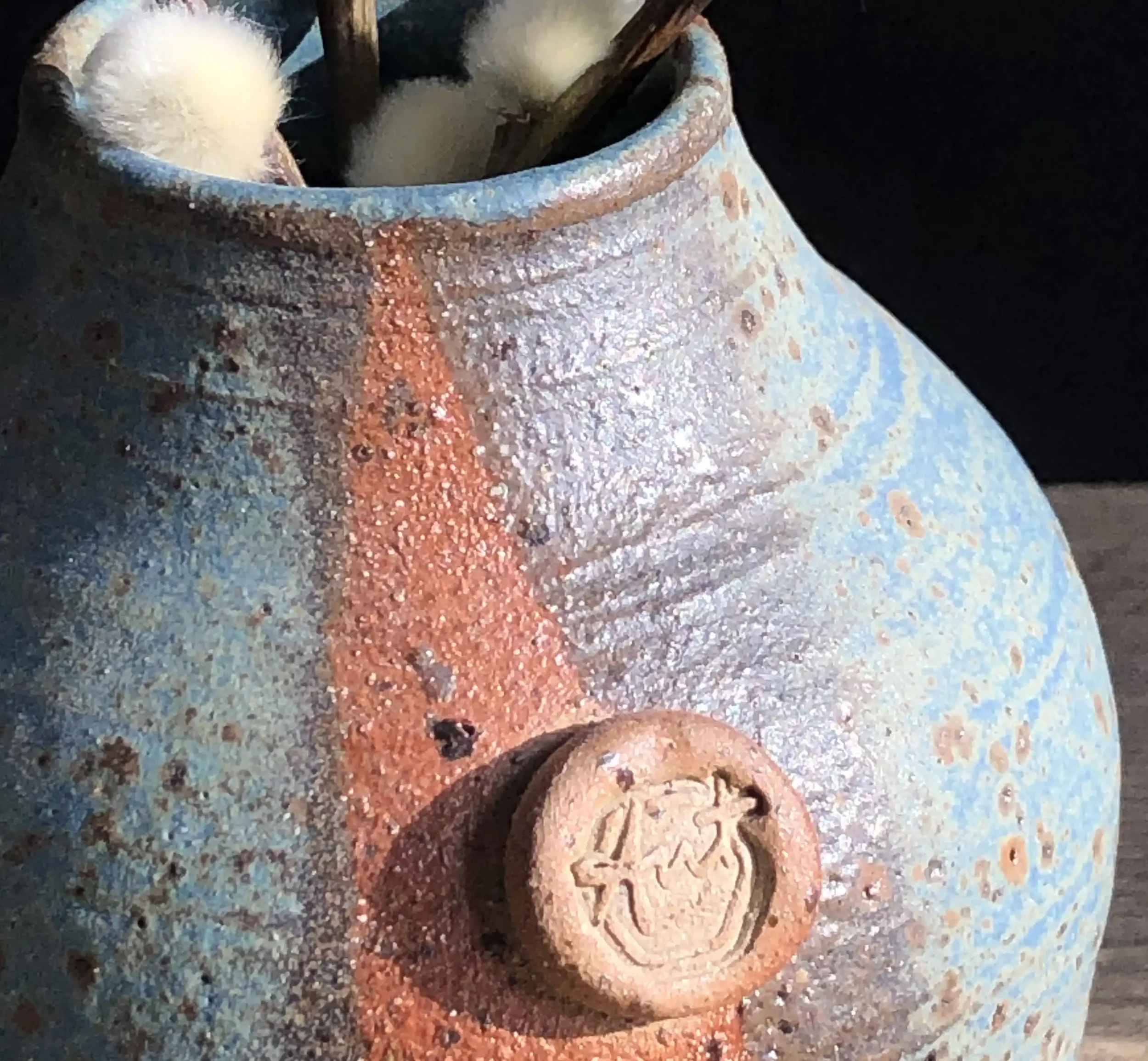 Close-up of a rustic ceramic bud vase with a textured surface, featuring a small circular emblem with Ant Kelly Creations maker's mark stamp.