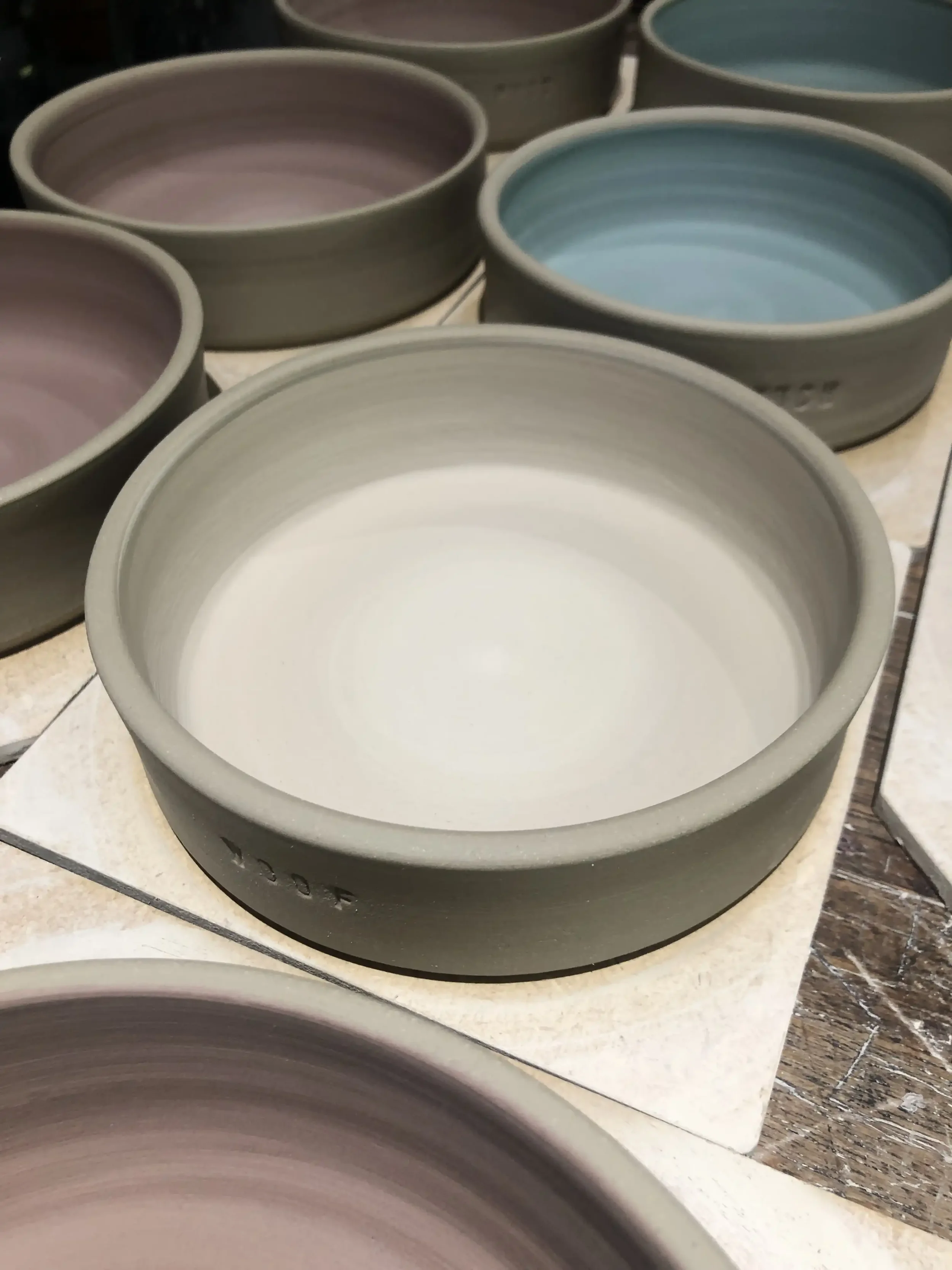 Unfinished ceramic bowls in various pastel colors on a worktable, in the process of being shaped and decorated.
