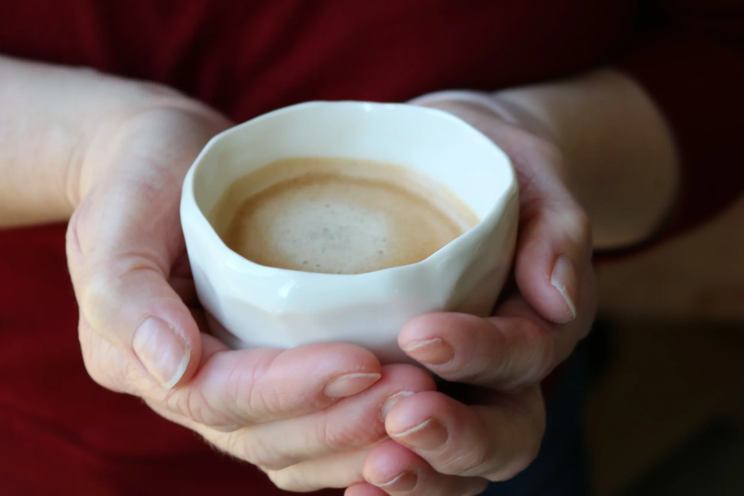 Person holding a white porcelain cup of coffee.