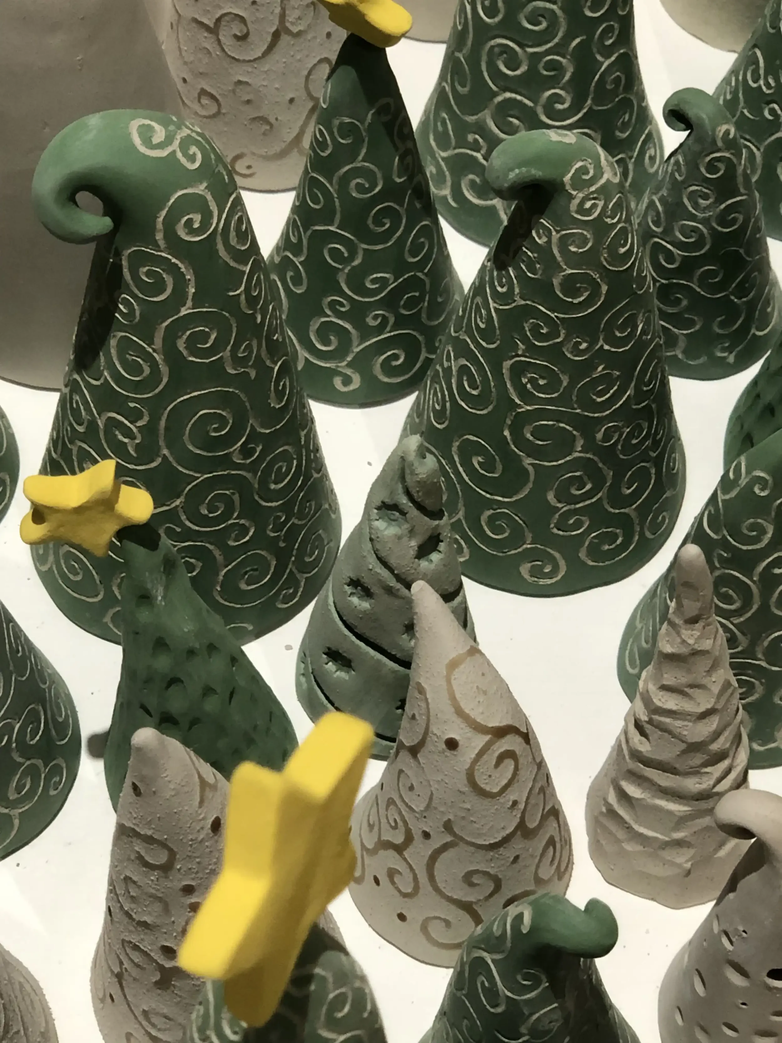 Collection of ceramic Christmas trees in various shapes and colours with swirly patterns and yellow accents.