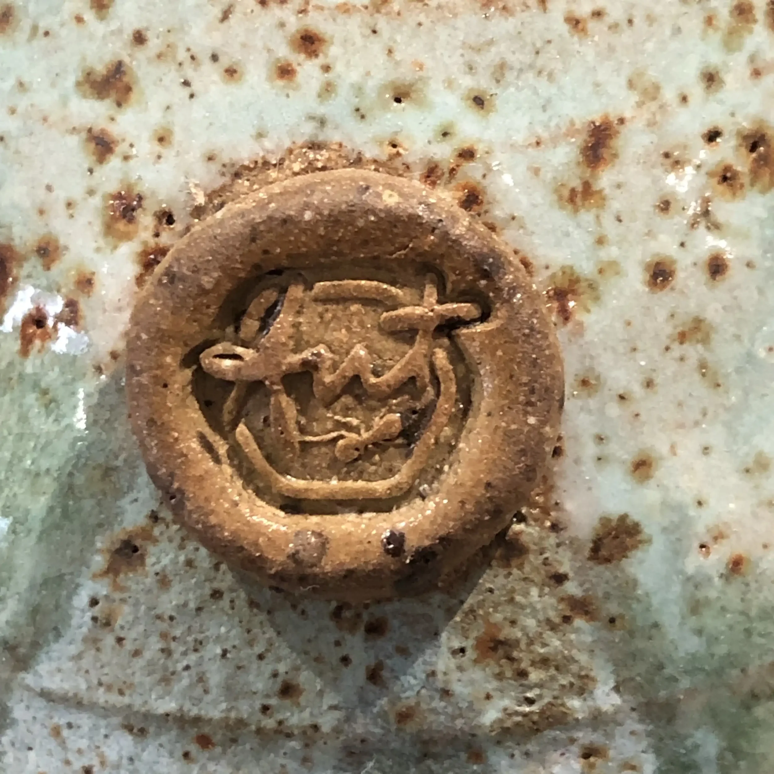 Close-up of Ant Kelly Creations maker's mark stamped into clay after being fired and glazed.