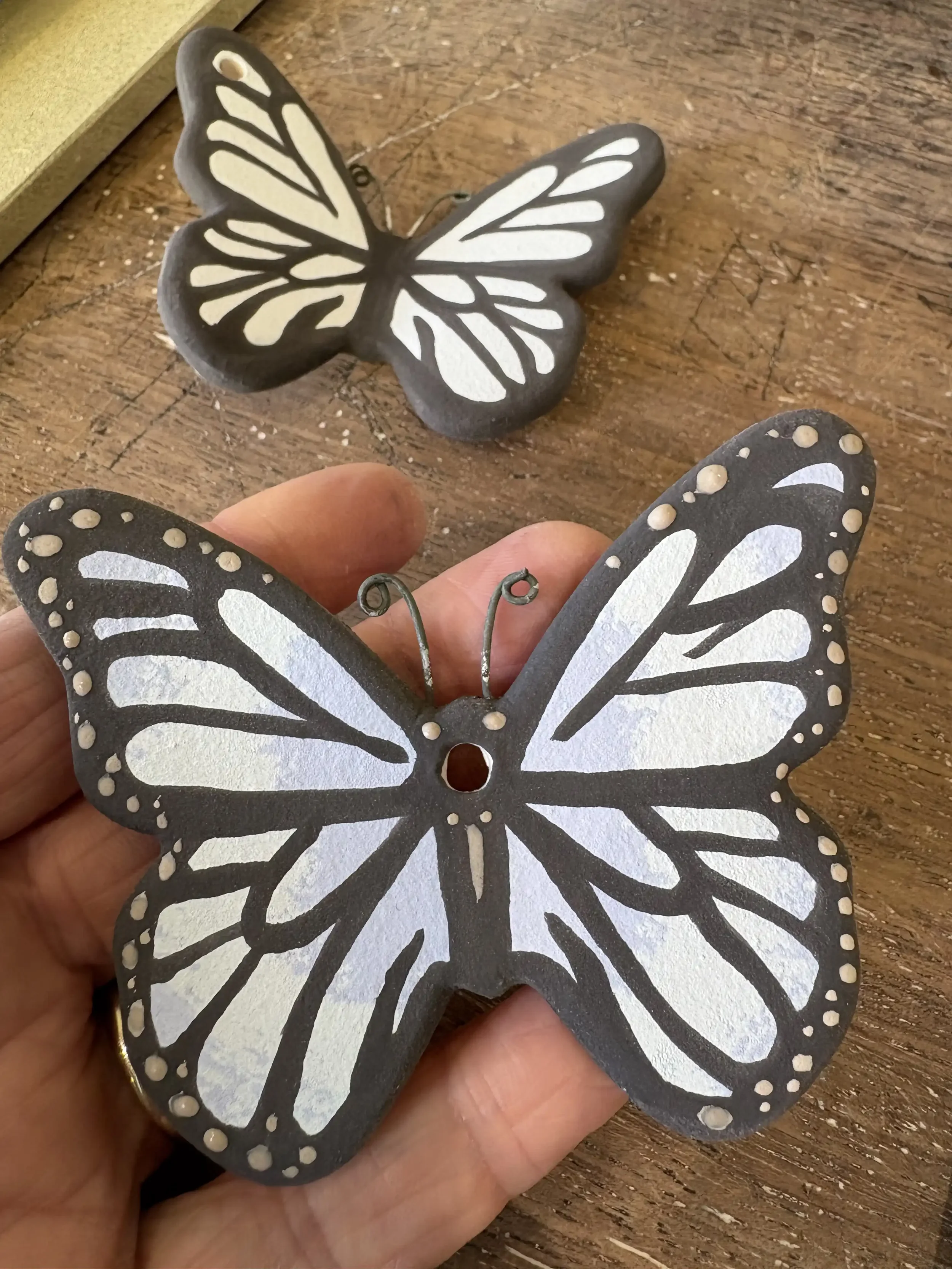 Decorative butterfly ornaments with black and white patterns, one held by hand and one placed on a wooden surface.