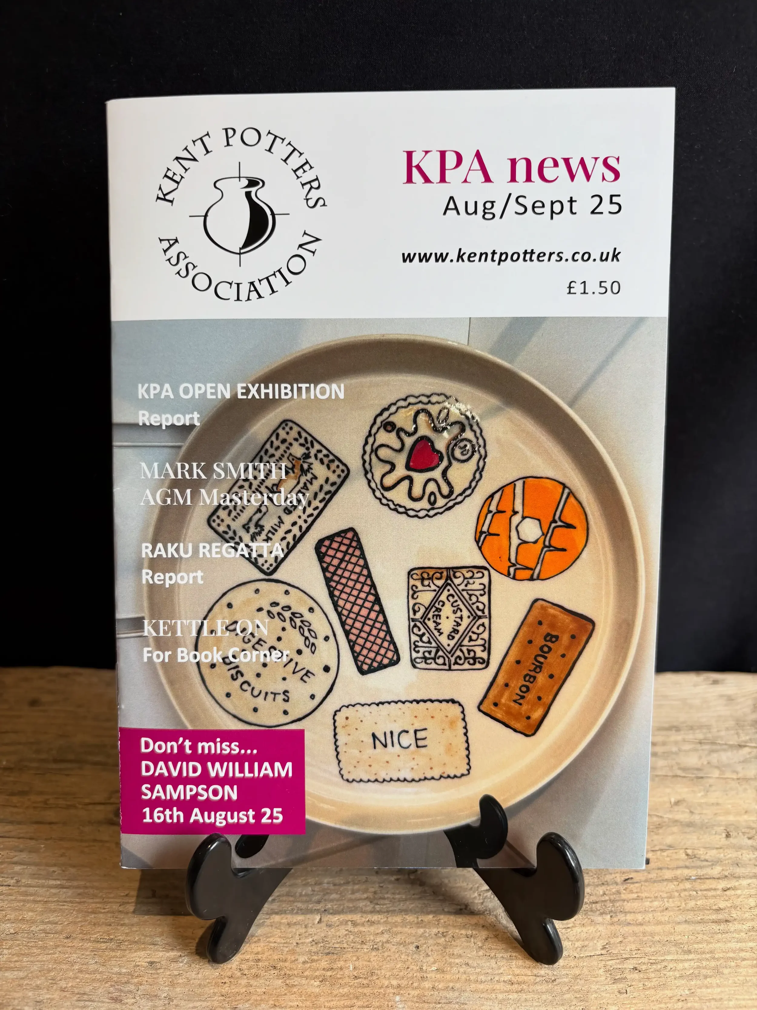 The cover of a newsletter from the Kent Potters Association, dated August/September 2025, featuring a photo of a plate decorated with popular British biscuits including a Custard Cream, Jammie Dodger, Rich Tea Biscuit and Digestive Biscuit.