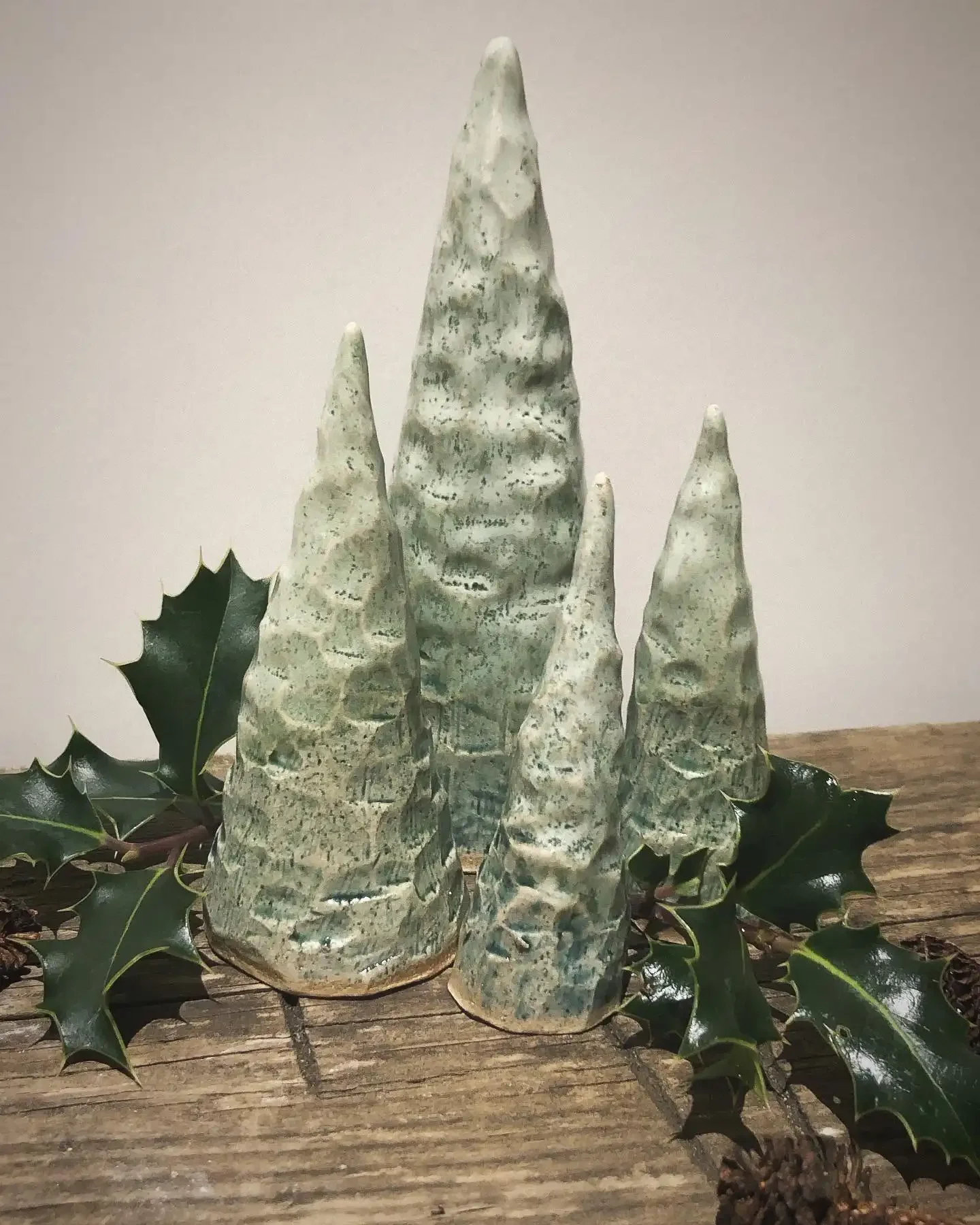 Decorative carved ceramic sculptures resembling Christmas trees surrounded by holly leaves on a wooden surface.