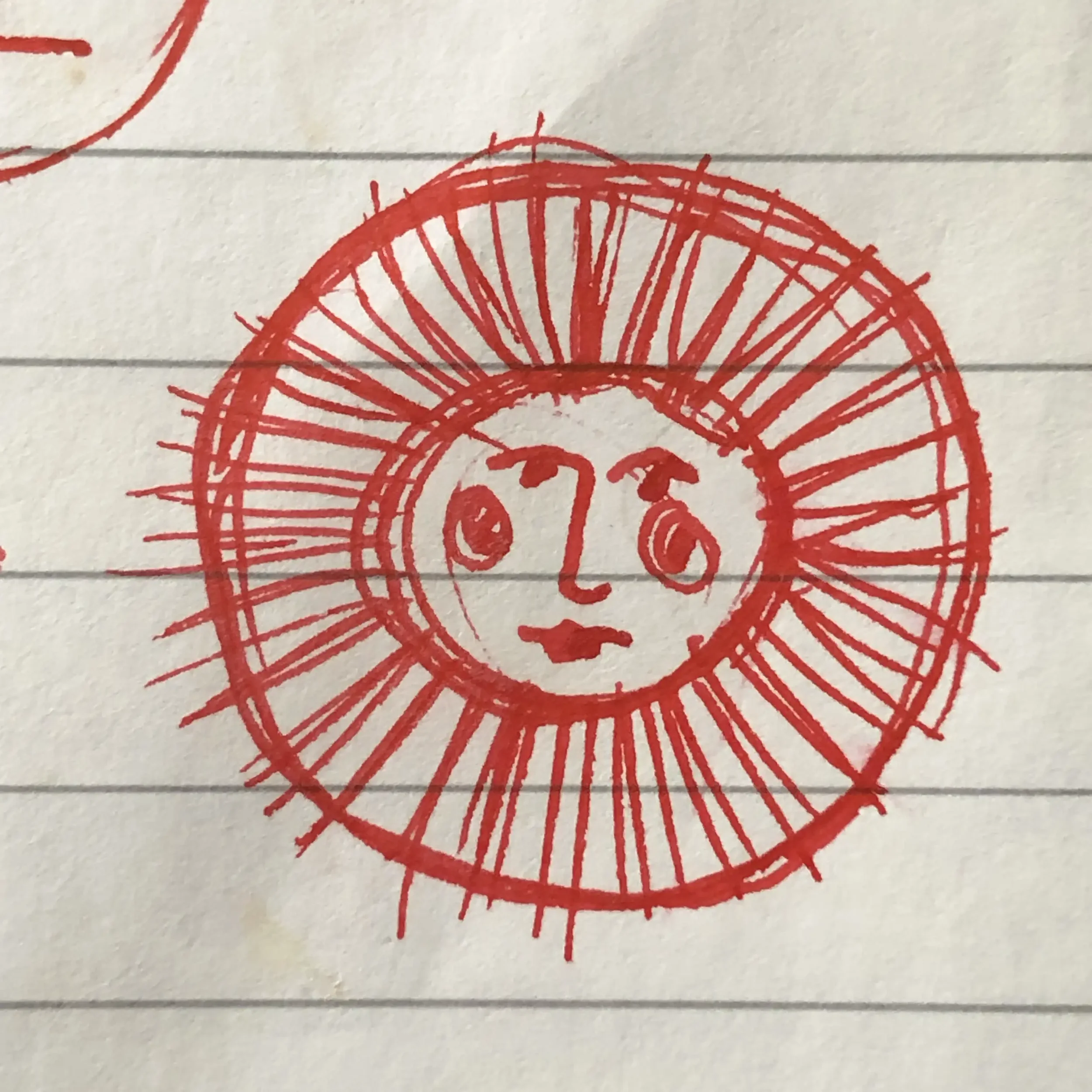 Hand-drawn sun with a face, surrounded by lines depicting rays, red pen on lined paper.